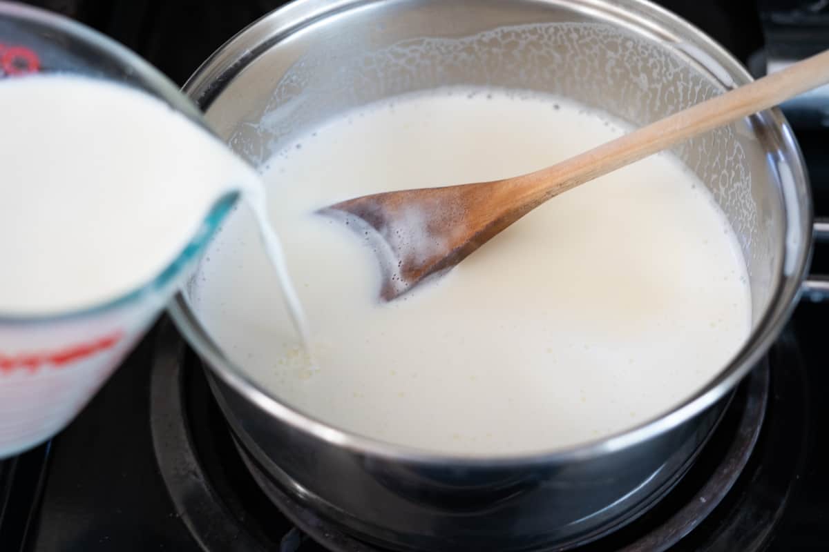 Pouring mixed corn starch with milk over the milk and sugar in a pot