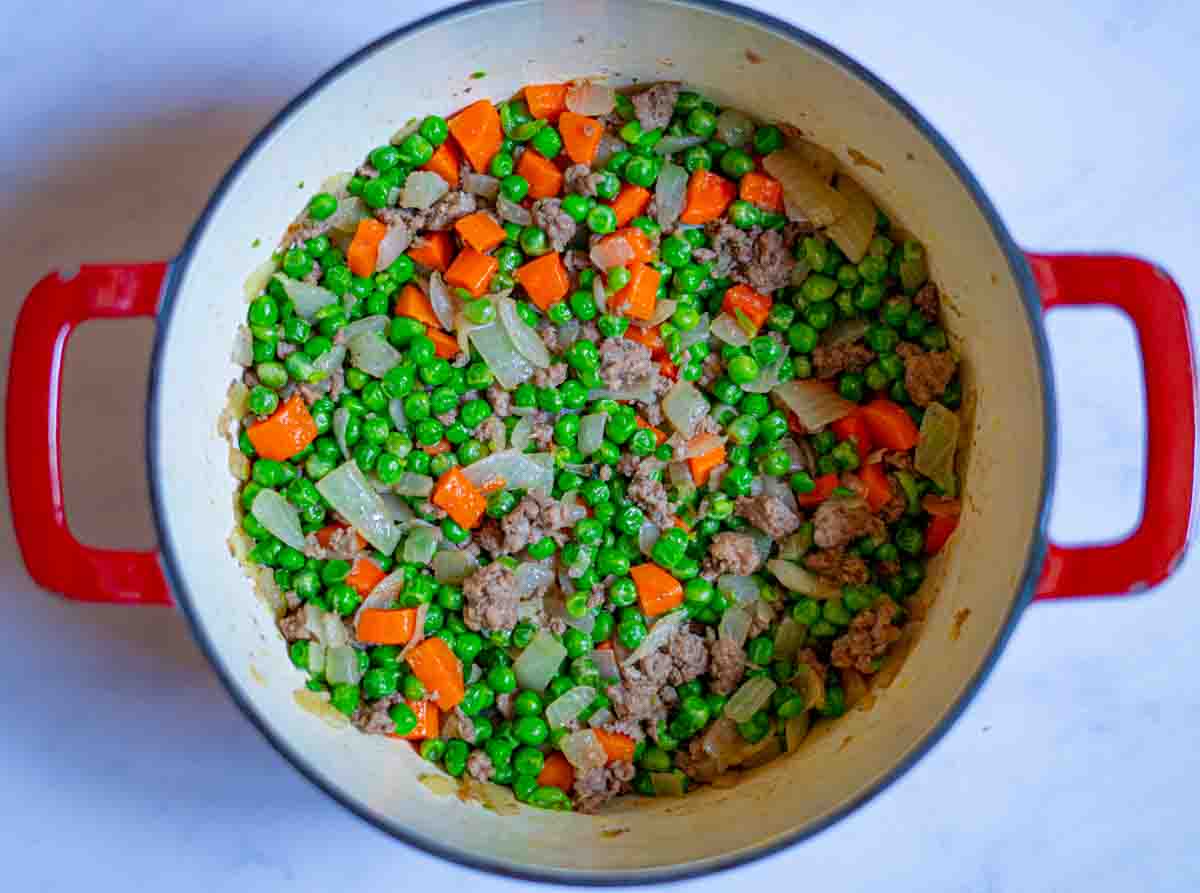 Peas, carrots and cooked meat with onions mixed in a pot