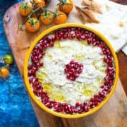 Close up photo of mutabal on a plate decorated with pomegranate seeds and a drizzle of extra virgin olive oil.