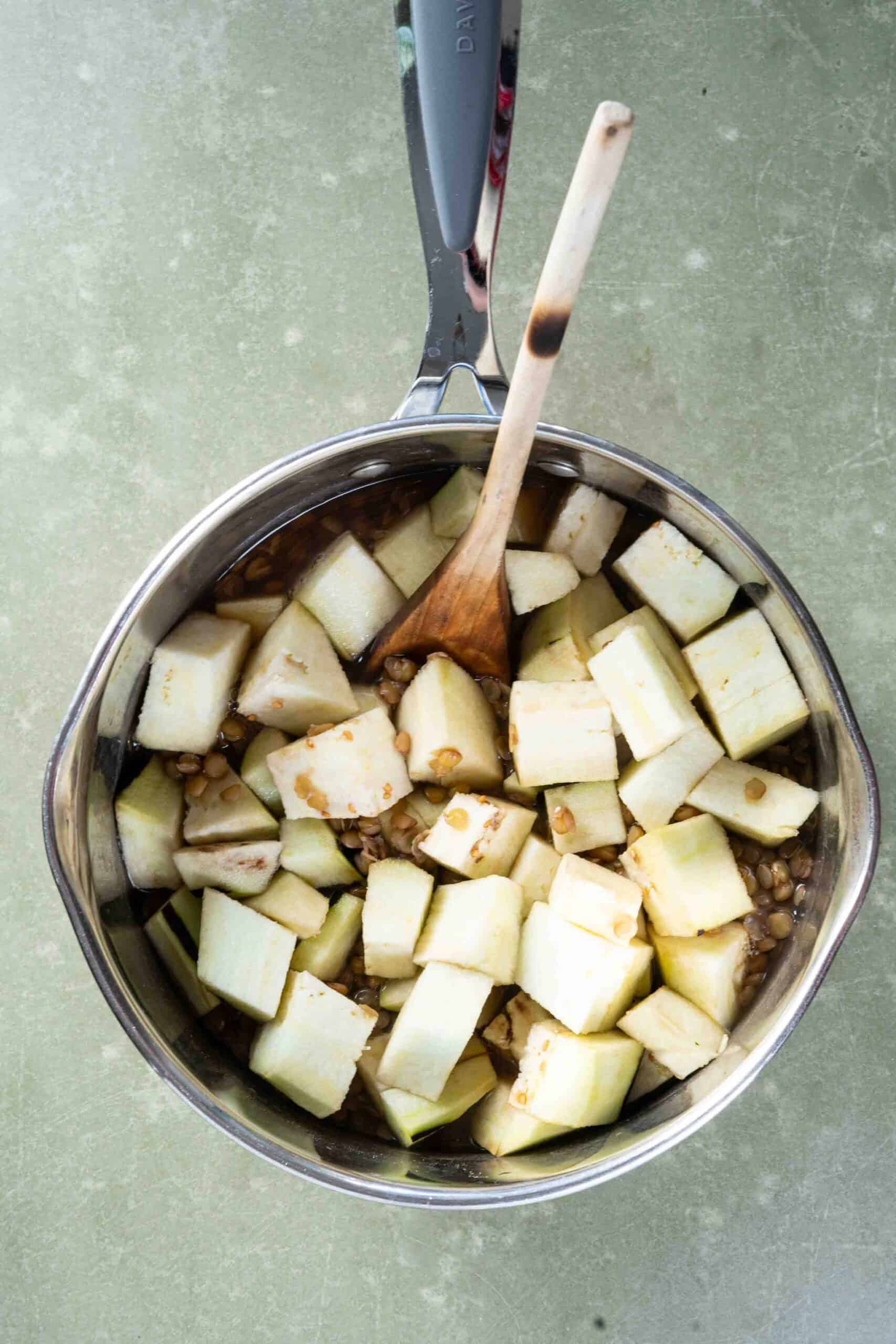 Chopped and peeled eggplant over cooked lentils in a pot
