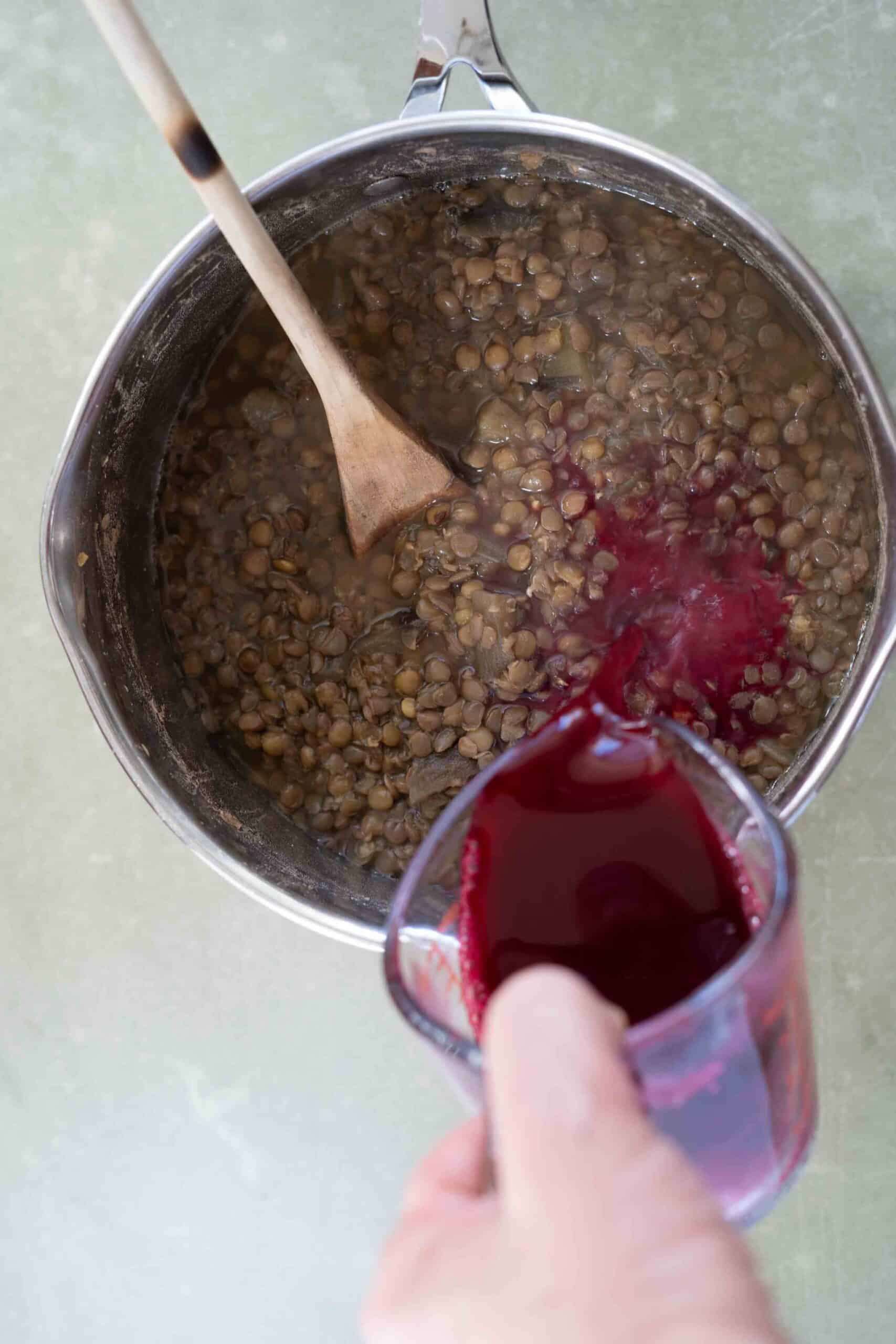 pouring pomegranate juice and flour mixture over cooked eggplant and lentils