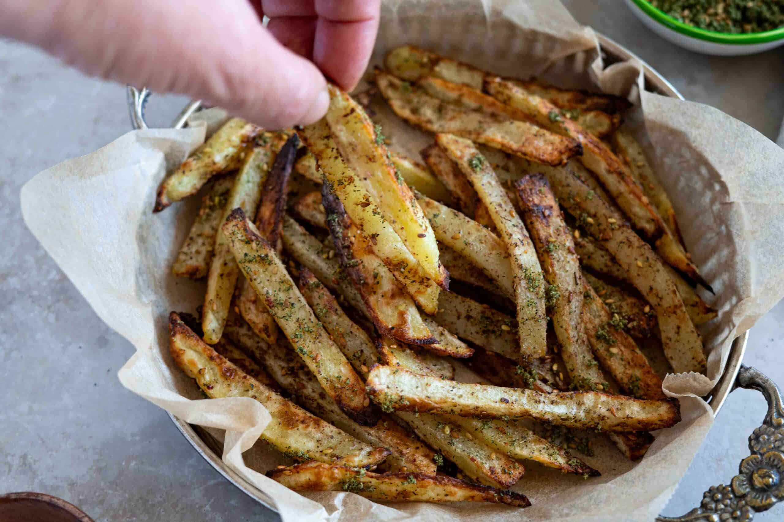 hand picking zaatar fries from a serving plate