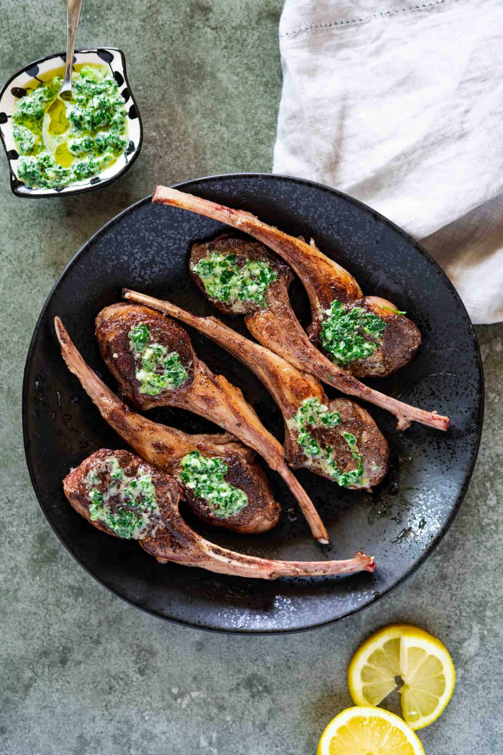 lamb chops on a plate with a side plate of garlic parsley paste.