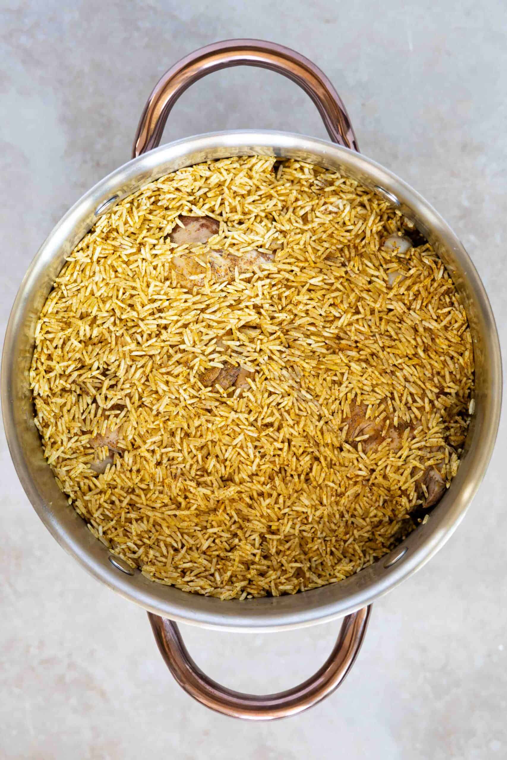Mixed rice with spices over all layers of vegetables before cooking in the pot.