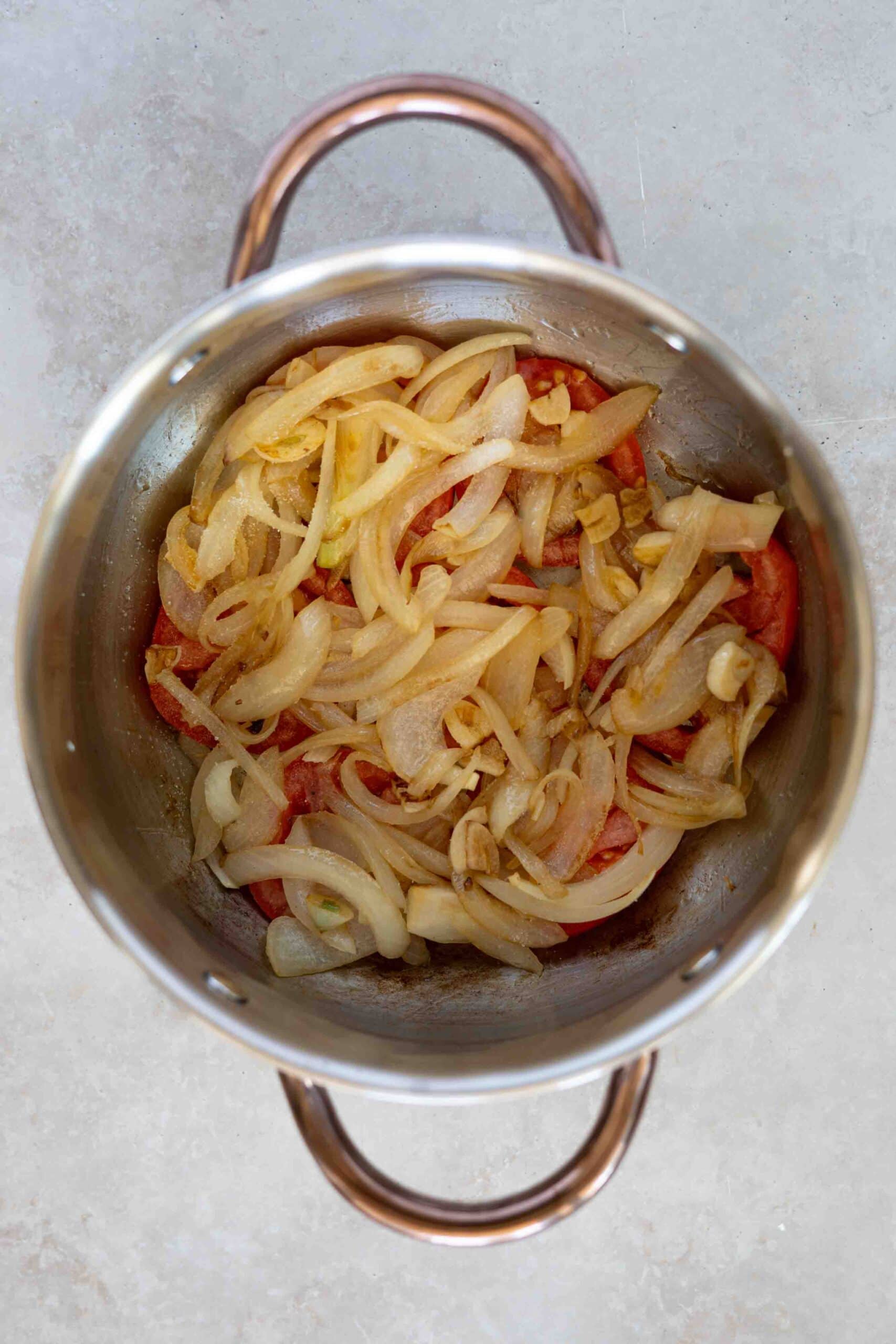 Sautéed onions and garlic over tomatoes in pot