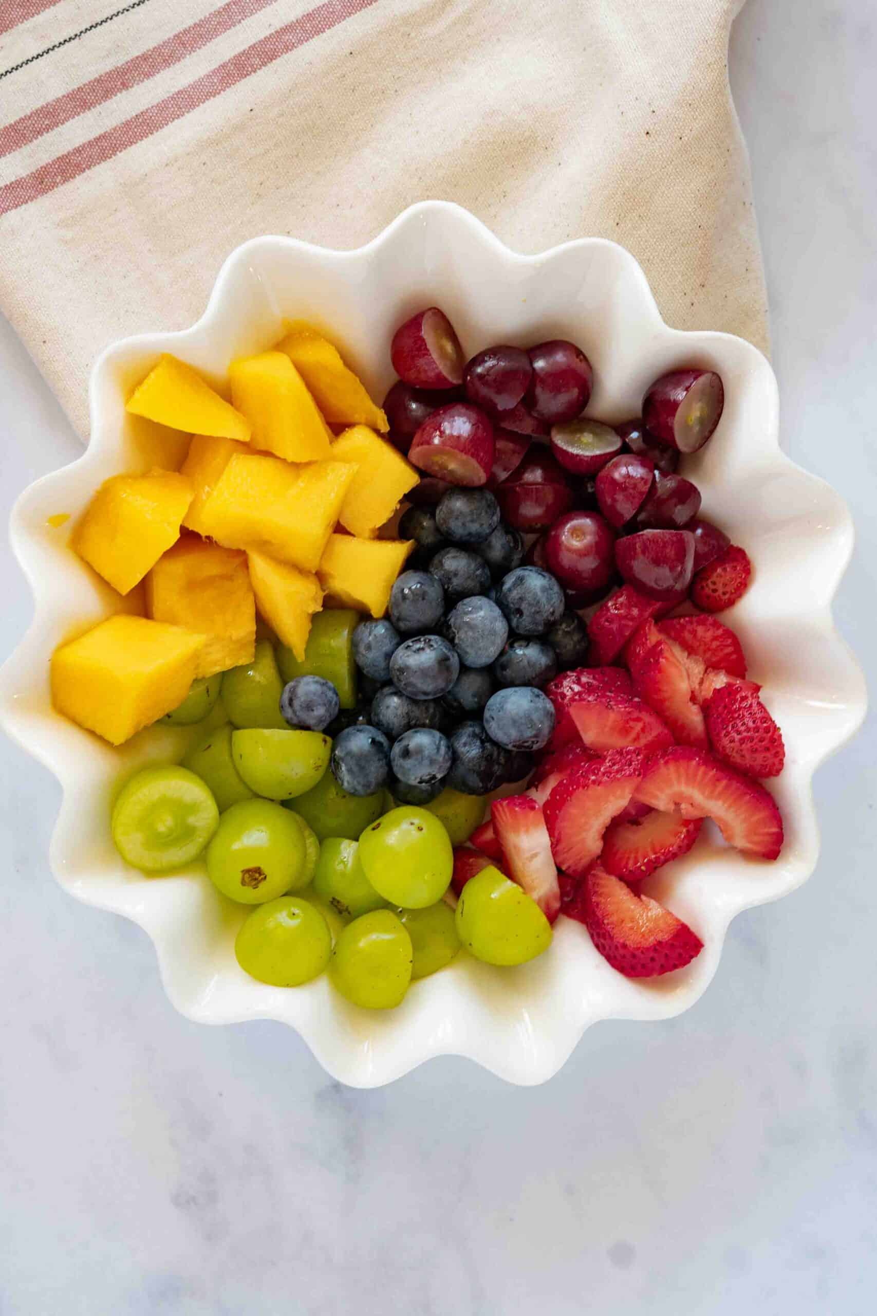 sliced mango, sliced grapes, sliced strawberries and berries all next to each other a bowl