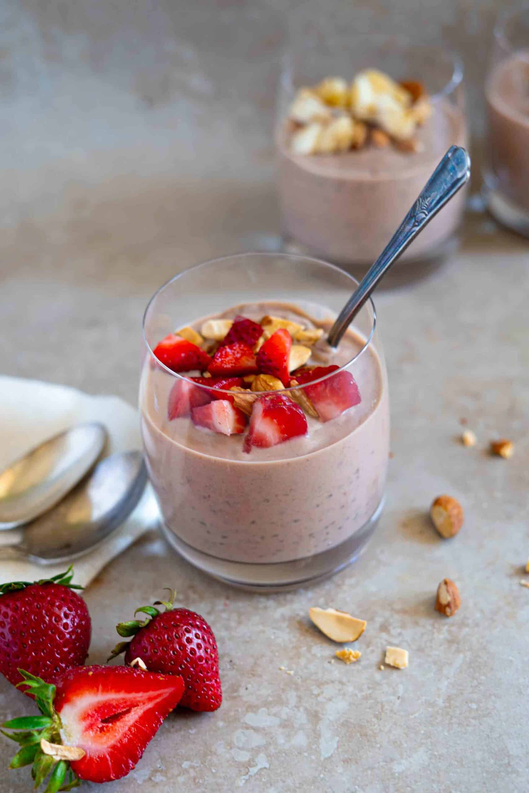 Banana chia pudding in a cup decorated with strawberry and toasted almonds on top, with a couple of strawberries on the side.