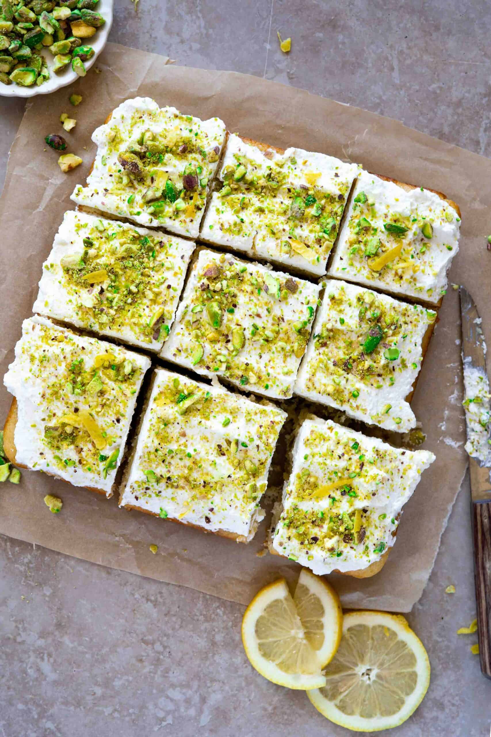 Cake covered with a layer of whipped cream and generously crushed pistachios then sliced into squares, about 9 pieces