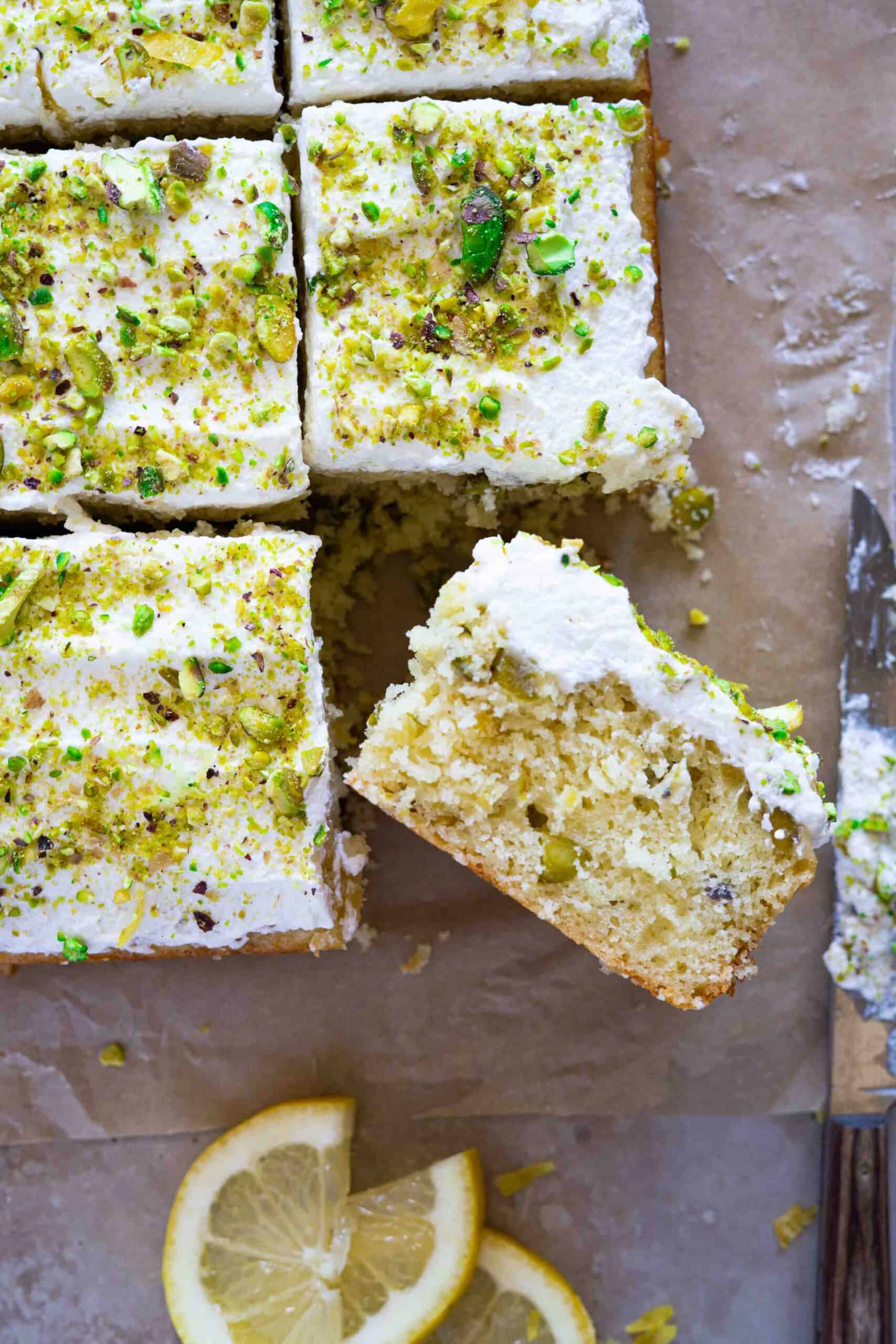 A close-up of a single slice of lemon pistachio cake, flipped on its side to show the soft, moist crumb dotted with crushed pistachios.