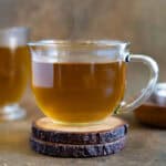 Anise hot tea served in a glass cup sitting on a wooden coaster. Feature photo