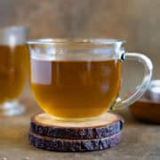 Anise hot tea served in a glass cup sitting on a wooden coaster. Feature photo