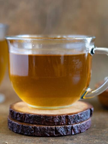 Anise hot tea served in a glass cup sitting on a wooden coaster. Feature photo