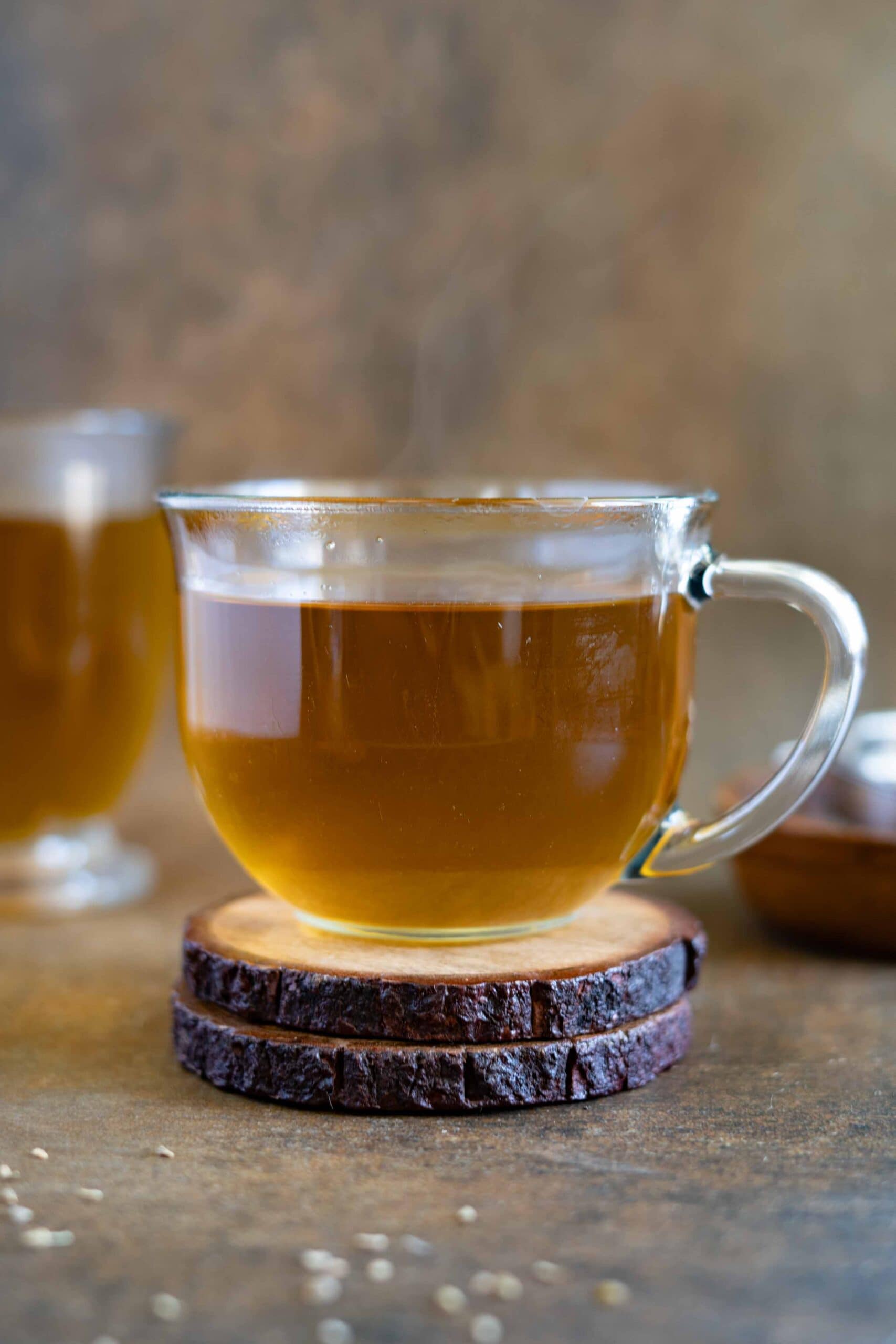 Warm Arabic herbal tea served in a clear glass cup on a wooden coaster.