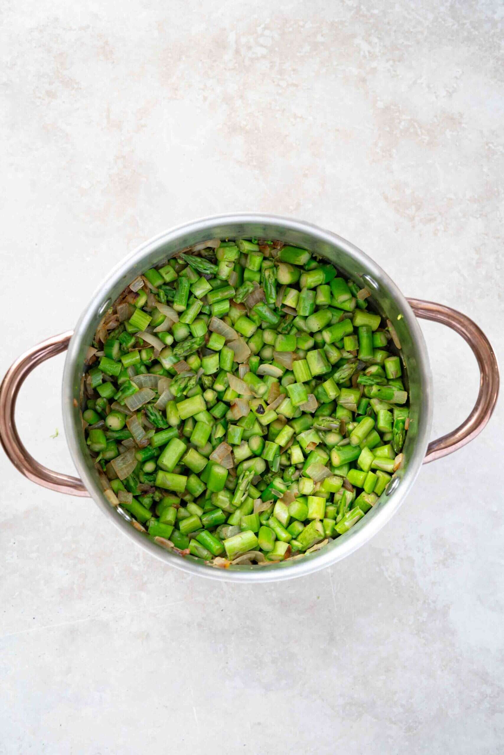 chopped asparagus over sautéed onions in a pot