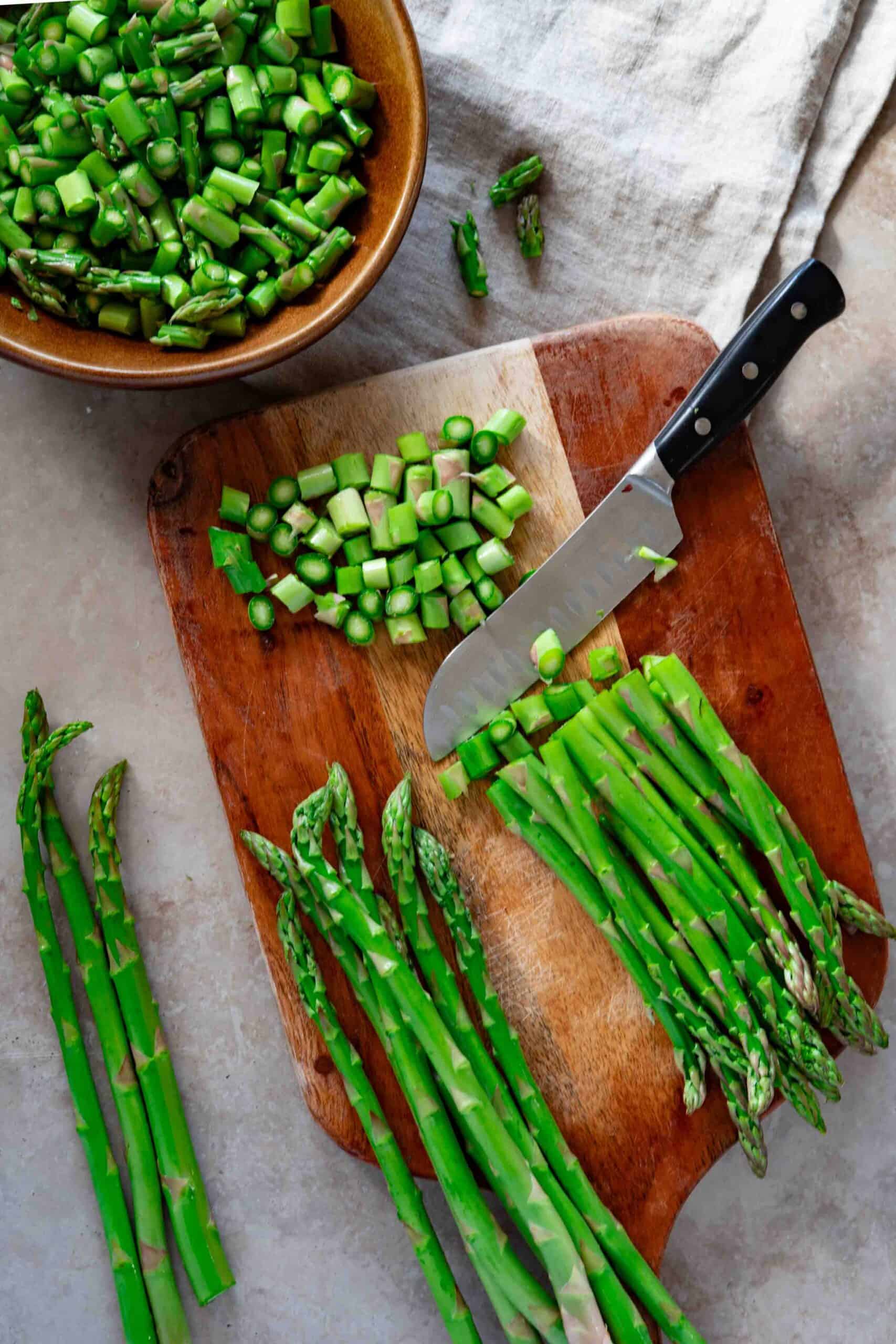 chopping asparagus on a chopping board, next to a bowl filled with chopped asparagus
