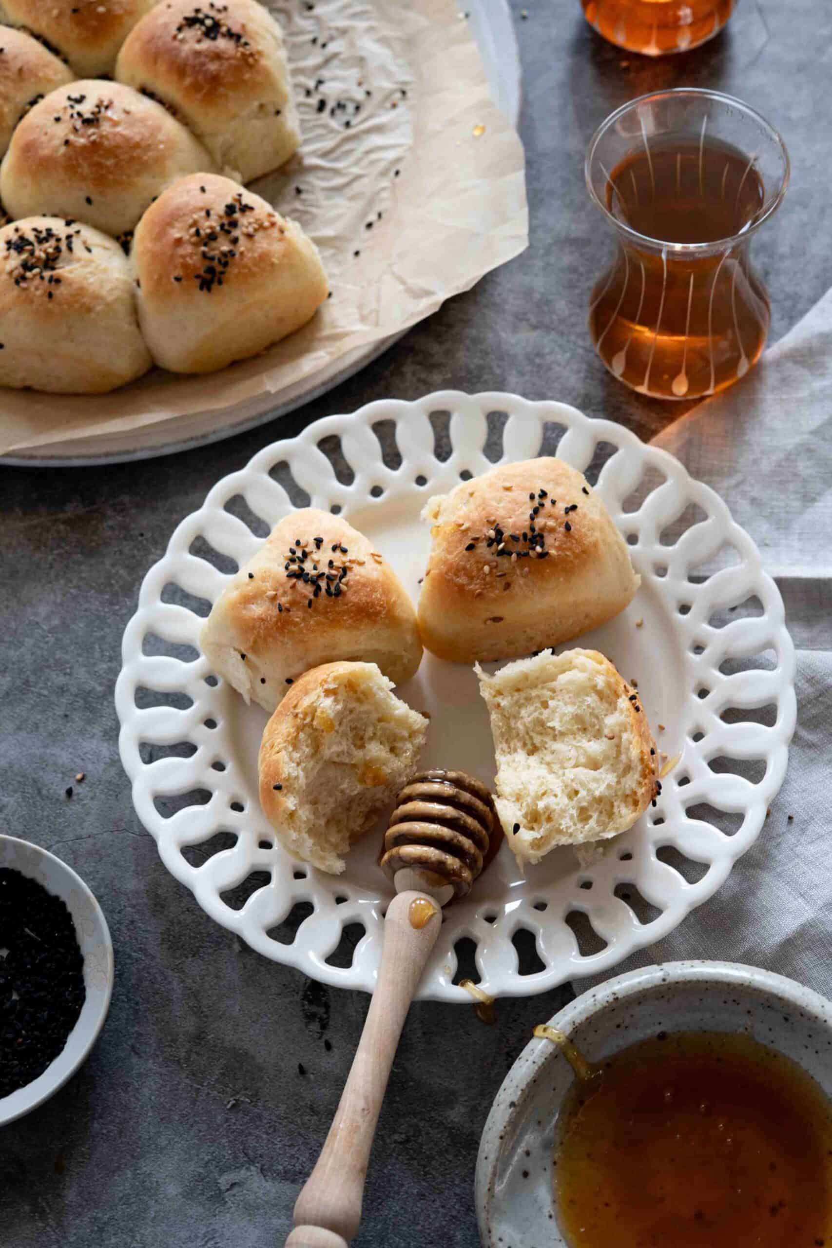 Honeycomb bread teared and placed on a plate with honey on the side, next to 2 cups of tea