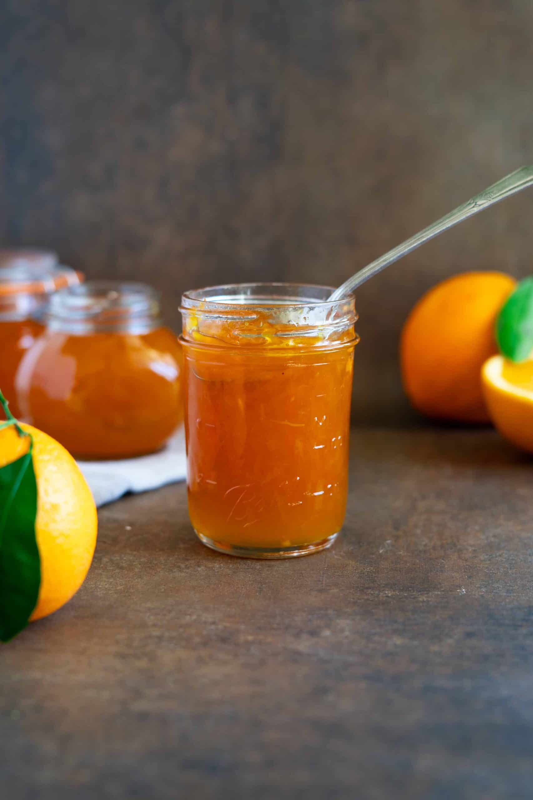 A jar filled with orange jam with a spoon dipped inside.