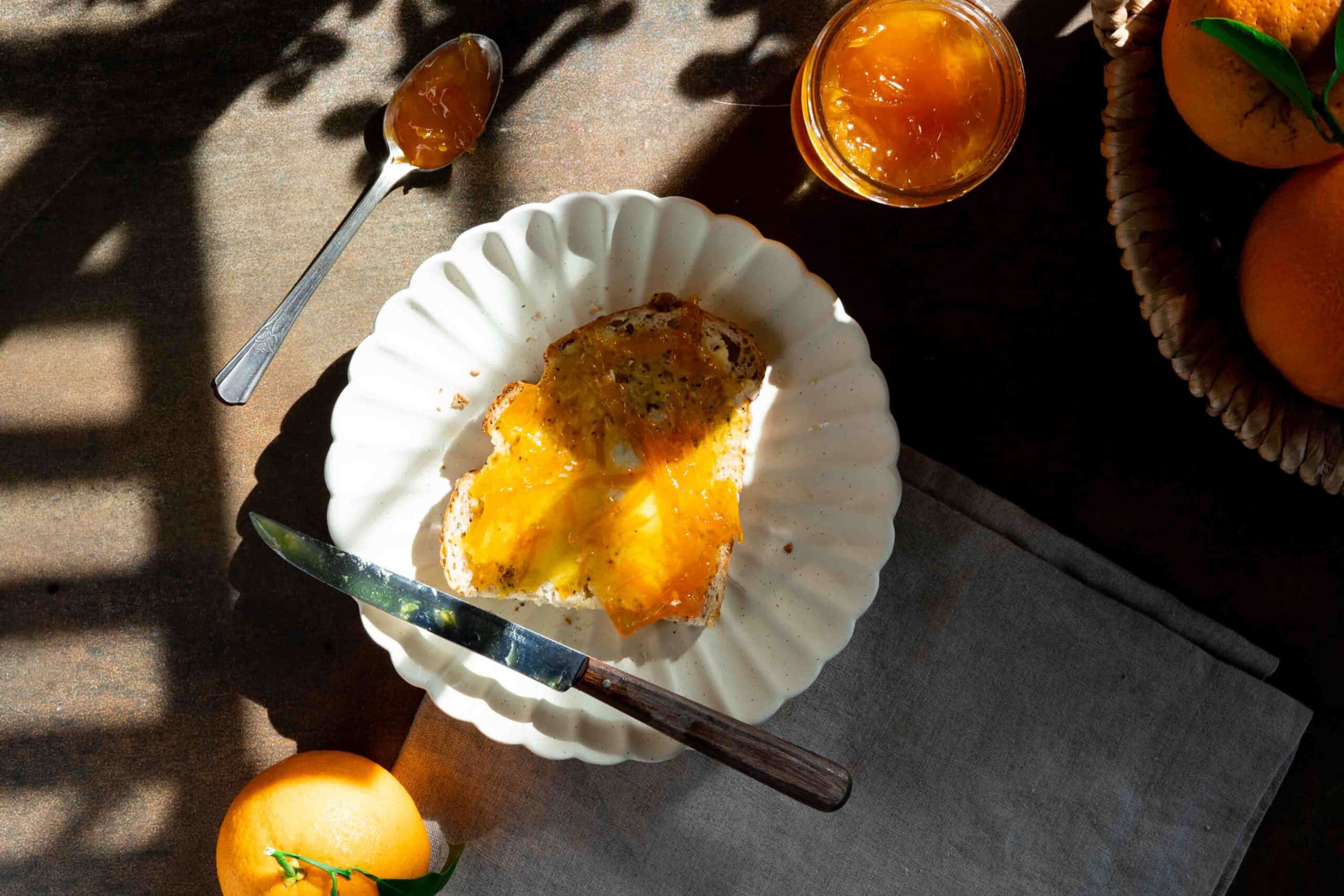 Orange jam spread on toast, placed on a plate, with an open jar filled with jam beside it.