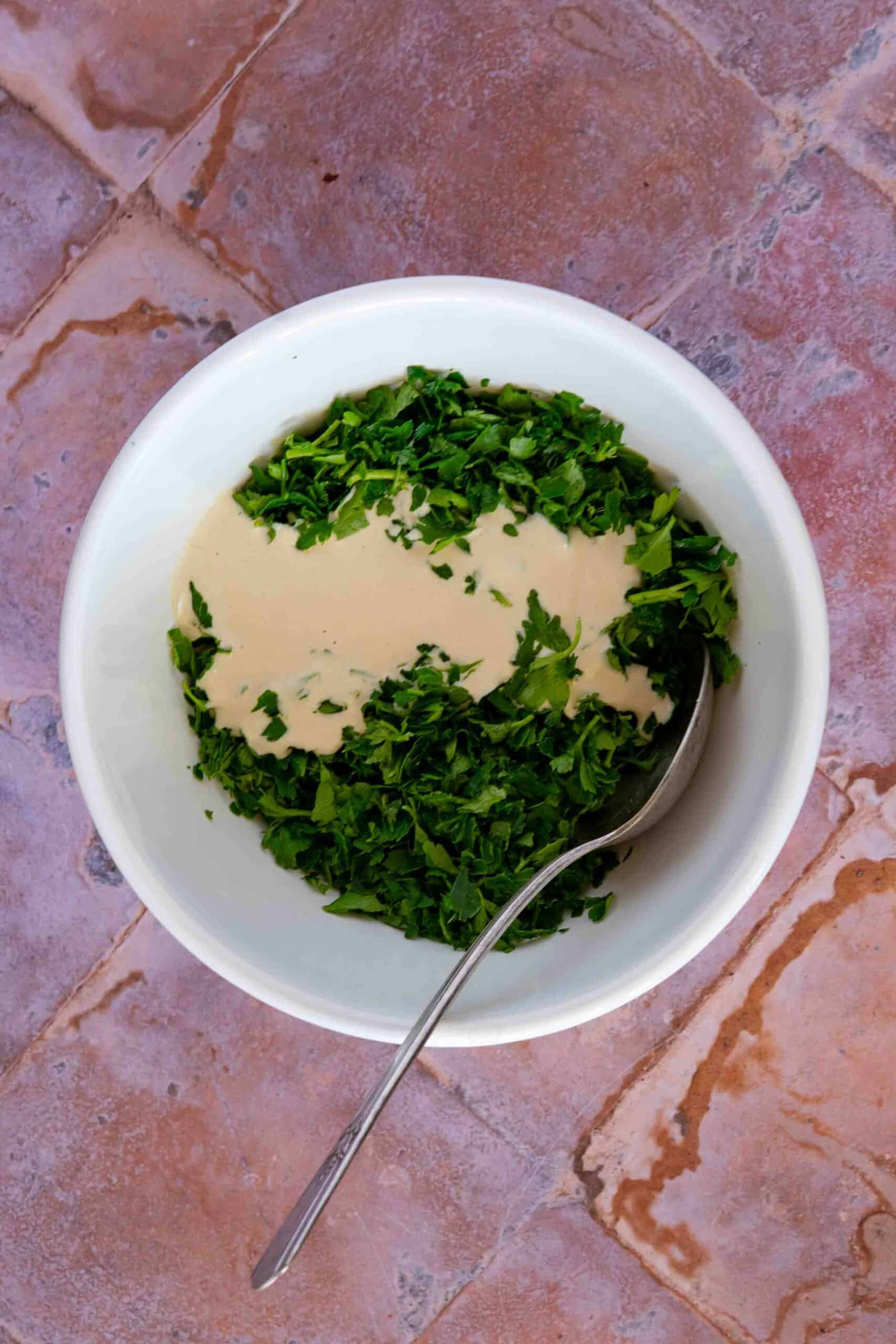 Pouring tahini sauce over chopped parsley