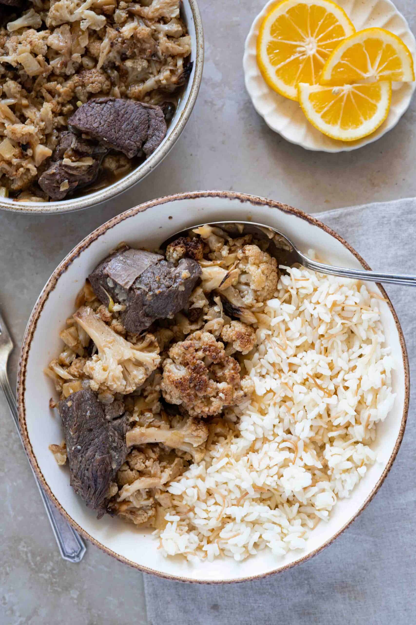 cauliflower stew in a serving plate next to vermicelli rice and slices of lemon.