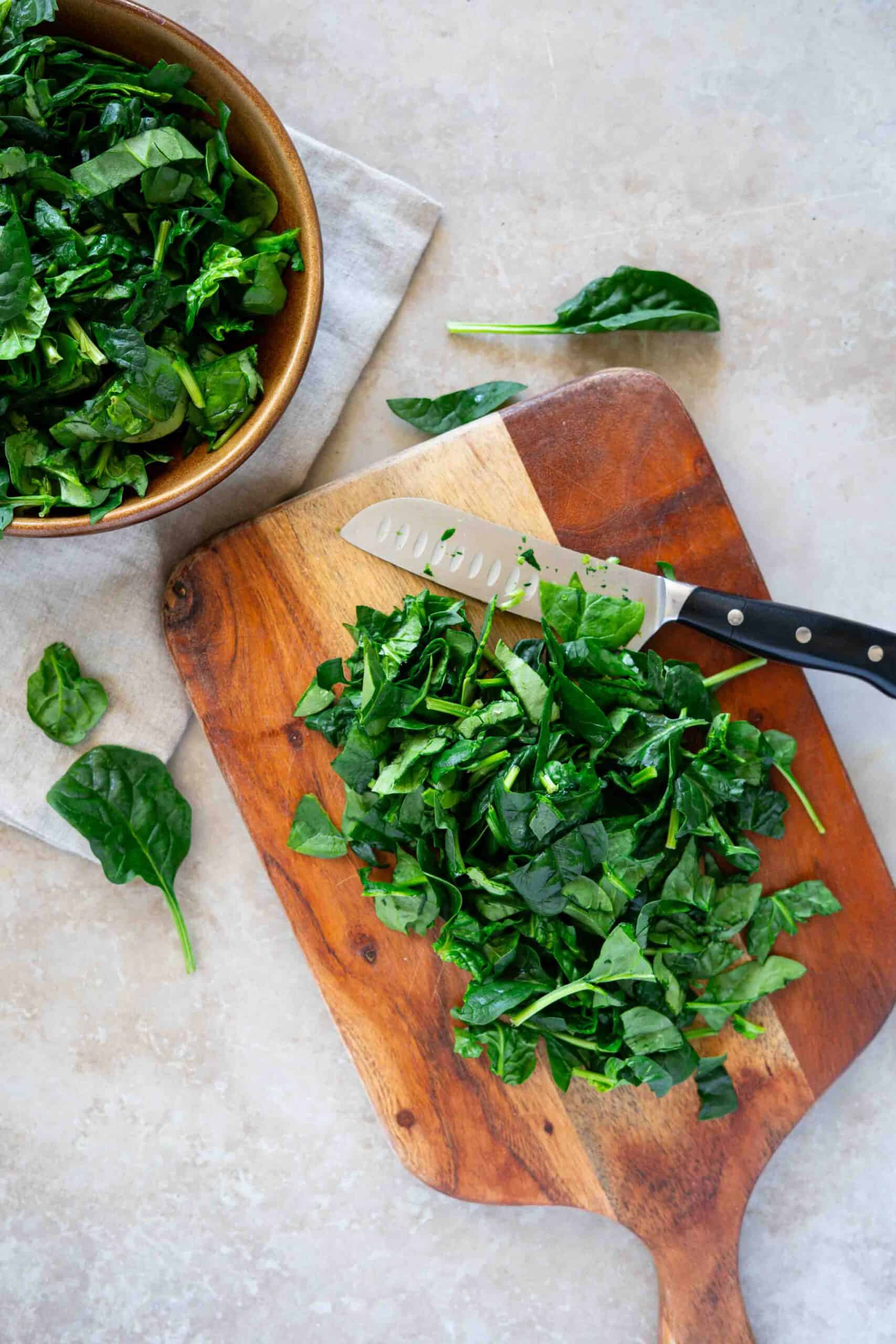 Chopping spinach using a sharp knife on a cutting board.