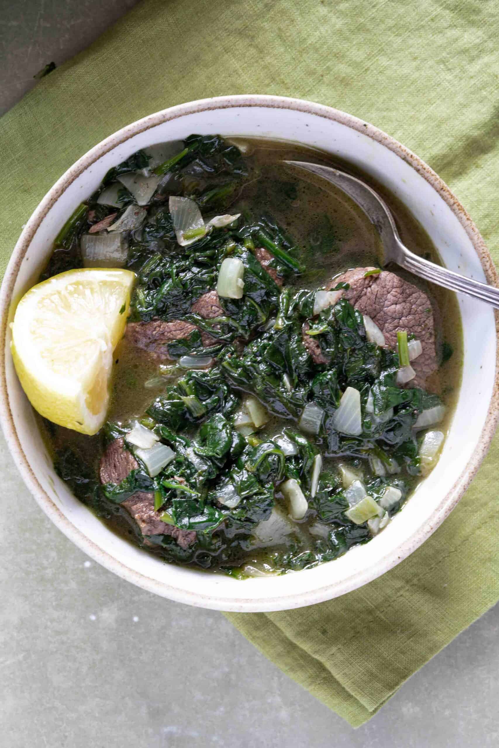 Spinach stew cooked with lamb in a bowl, with a slice of lemon.