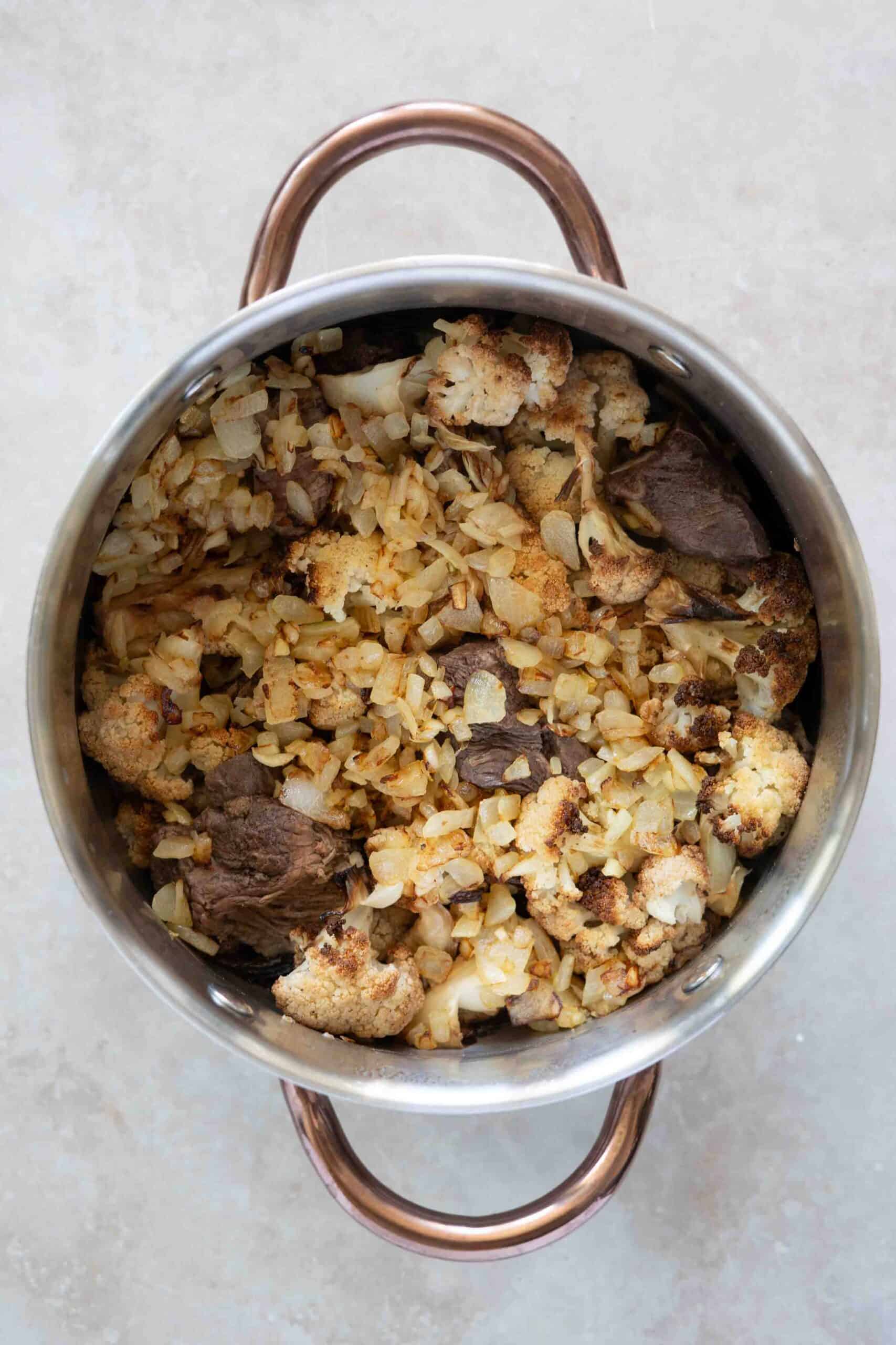 Pouring caramelized onion and garlic over cauliflower stew