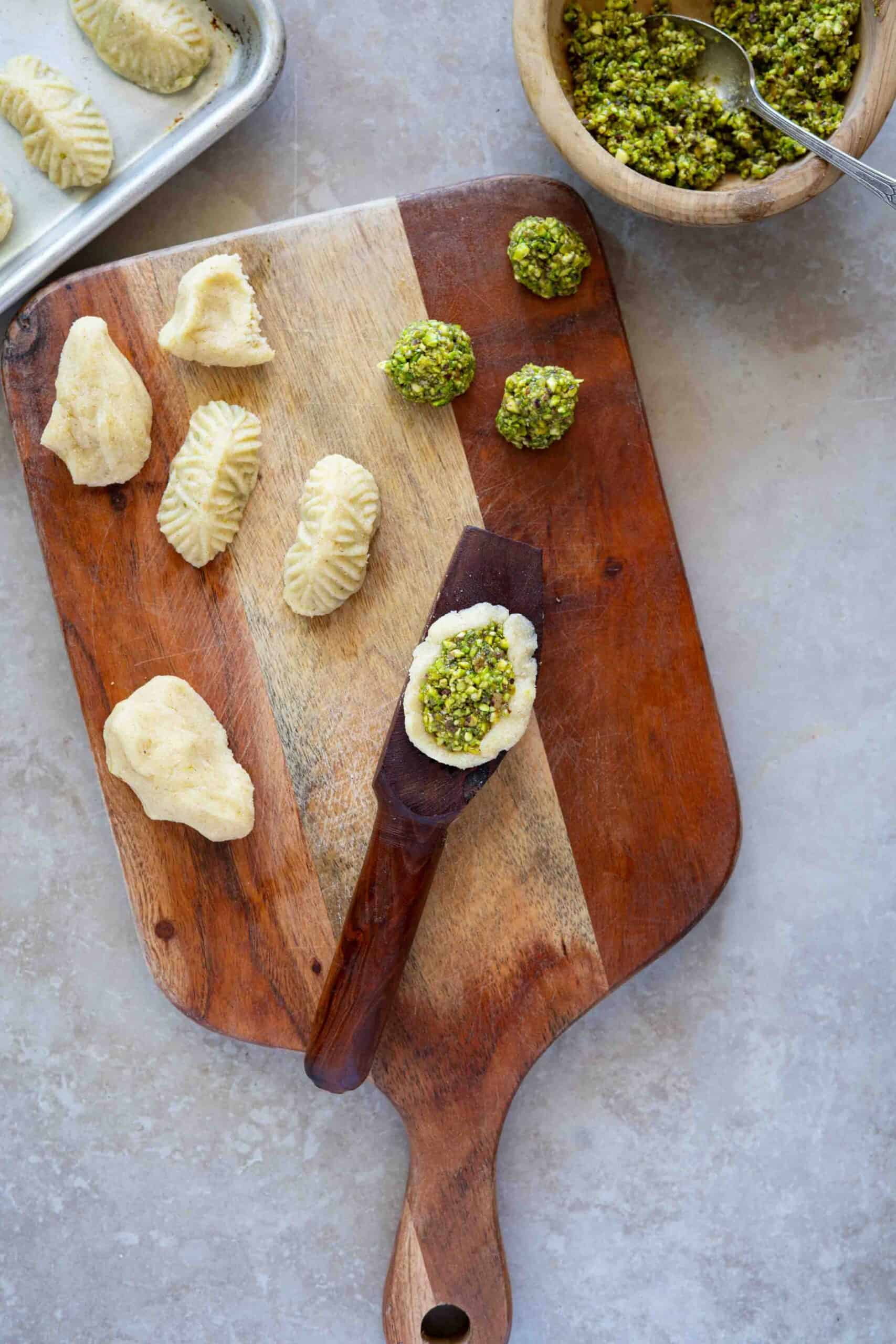 Step 1: Shape the cookies using a cookie mold. Fill the mold with a small piece of dough, pressing it into the mold to create space for the filling, then add the pistachio stuffing on top and press to seal it in.