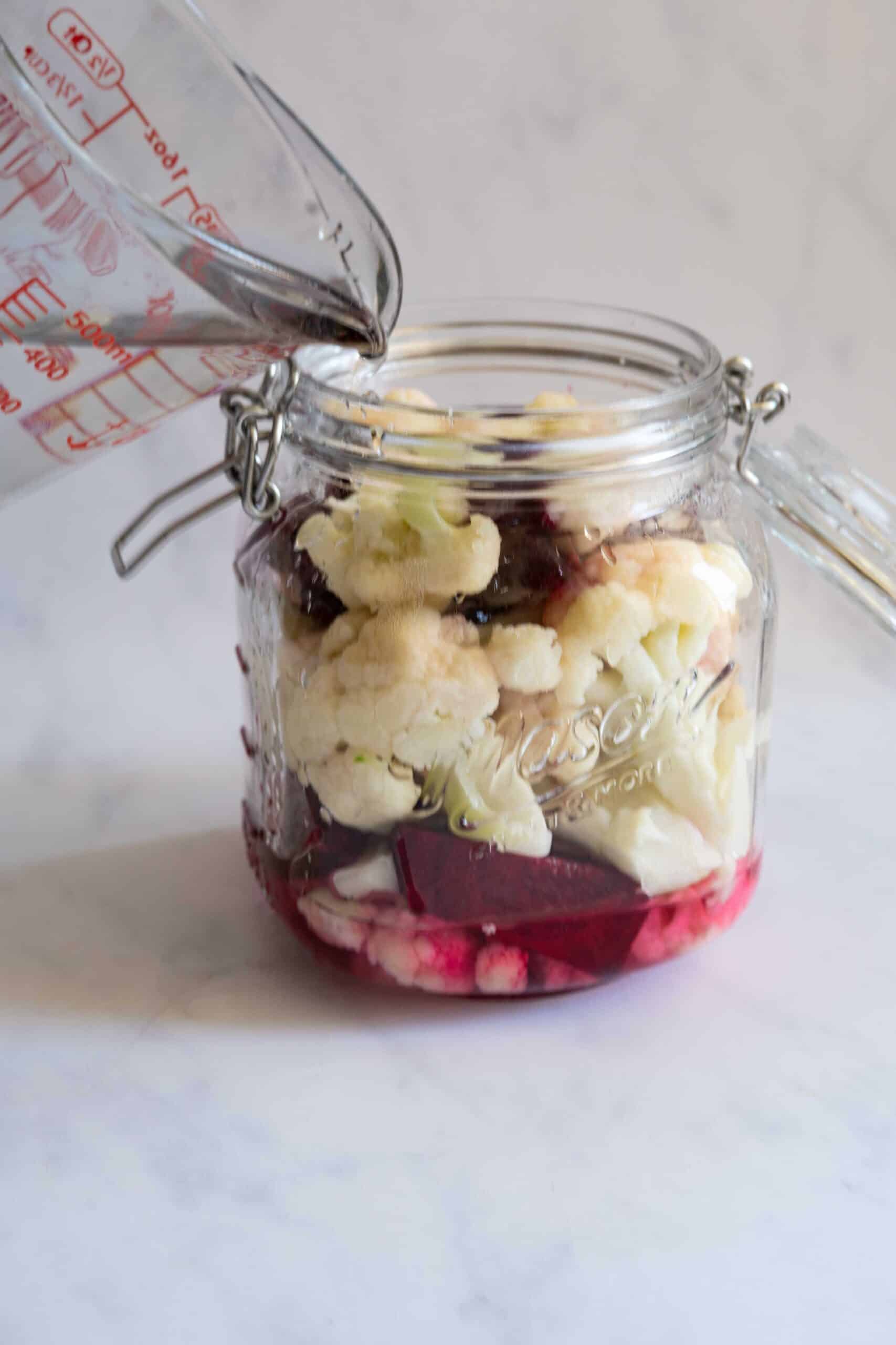 Pouring water with salt into a jar filled with cauliflower florets.