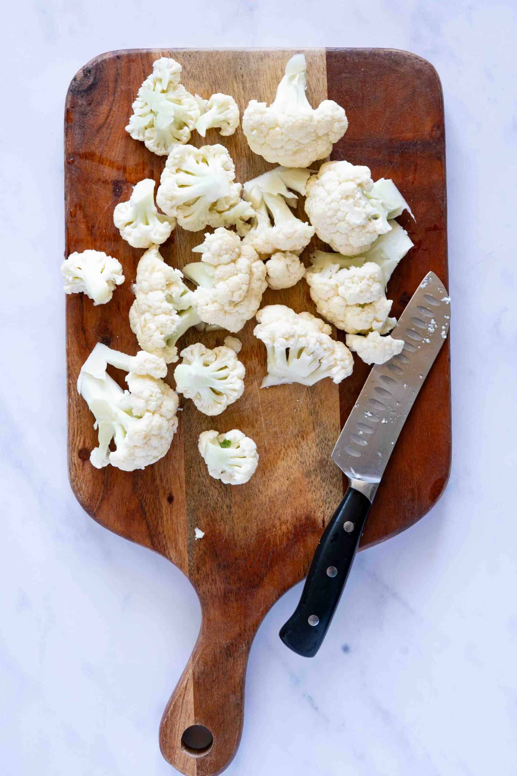 Cutting cauliflower into florets on a cutting board.