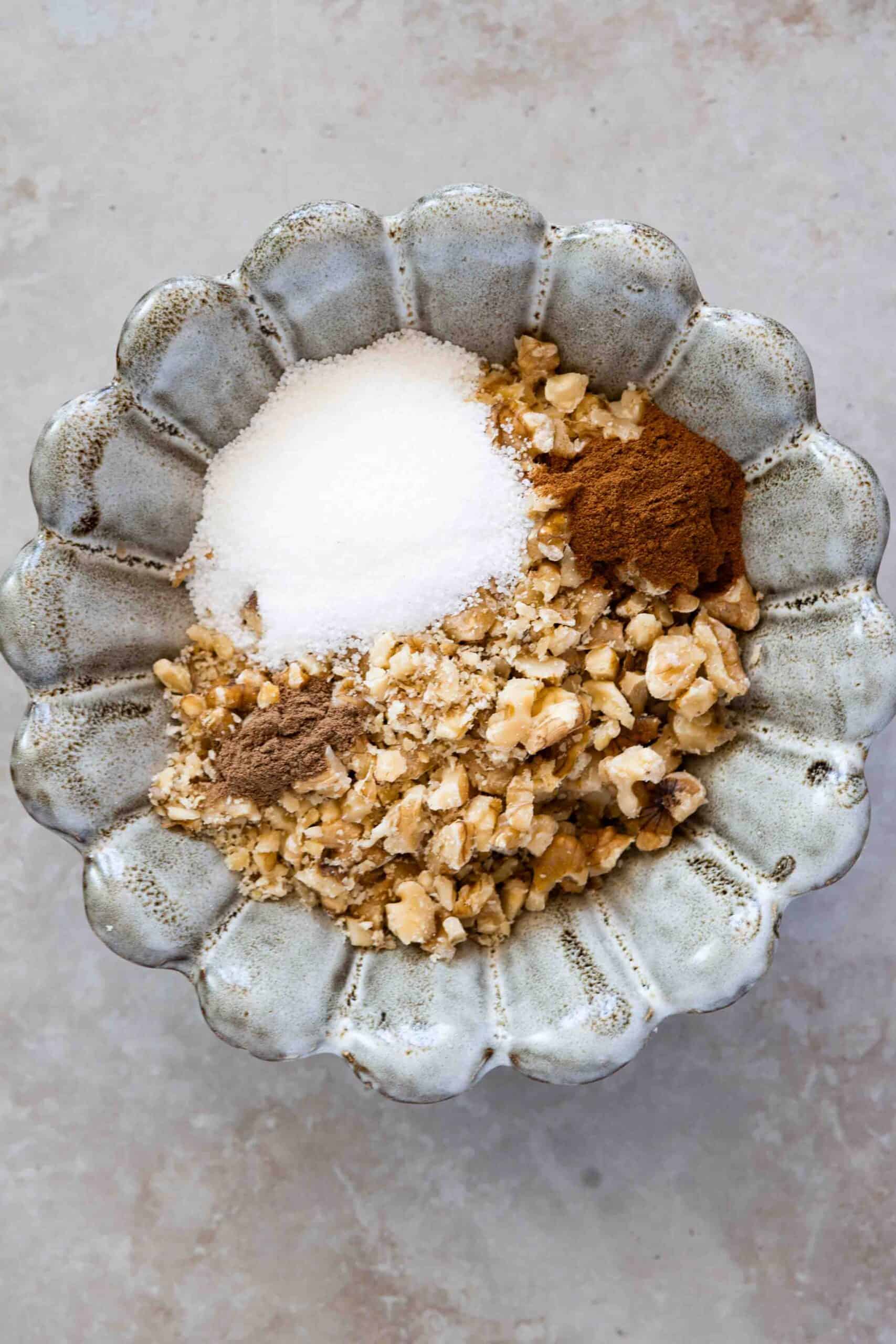 Chopped walnuts in a bowl with cinnamon and nutmeg powder and granulated sugar.