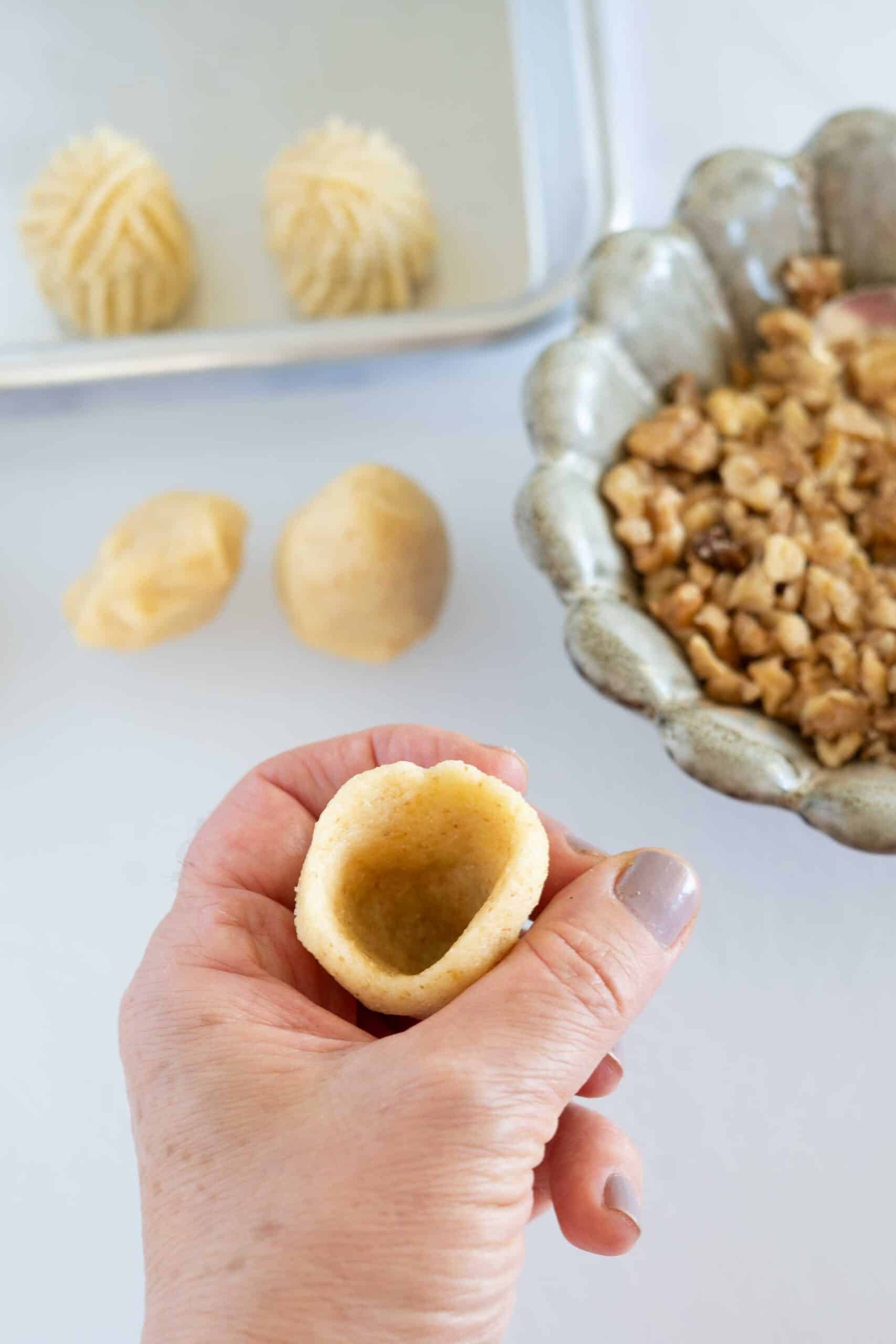 Shaping maamoul with walnut: Take a piece of dough about the size of your fist. Hold the dough in one hand and use the index finger of your other hand to make a hole in the center, shaping the dough into a dome or small cup.