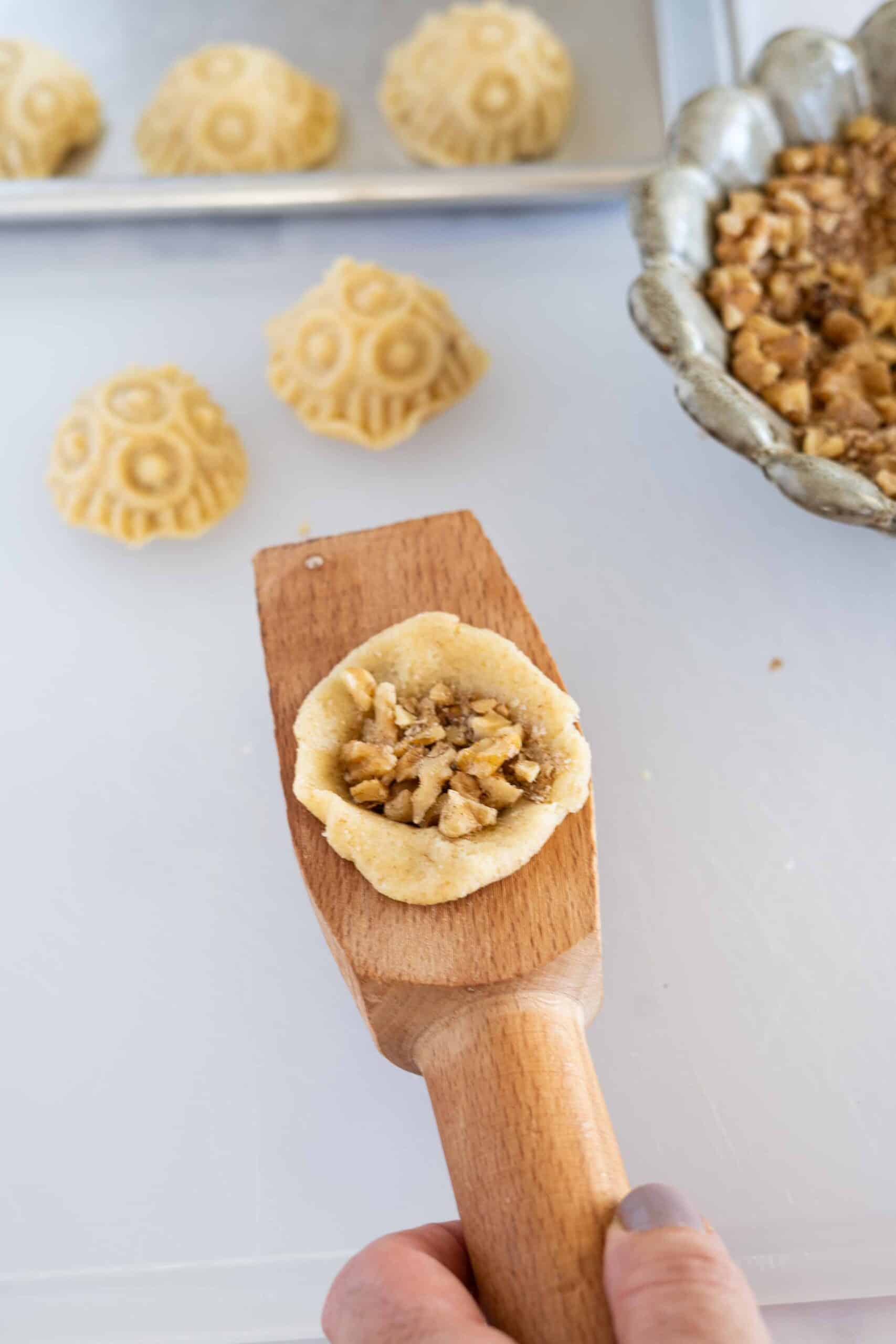 Take a piece of dough about the size of your fist and place it into the mold. Make a hole in the center and fill it with walnut filling.