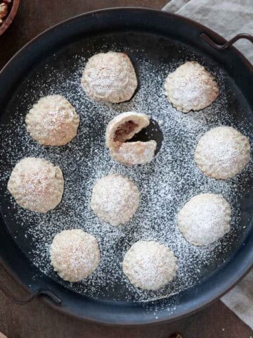 A close up photo for a rounded serving tray filled with maamoul, dusted with powdered sugar.