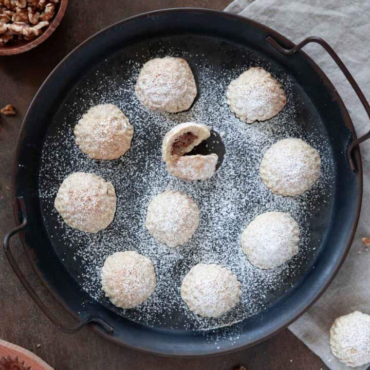 A close up photo for a rounded serving tray filled with maamoul, dusted with powdered sugar.