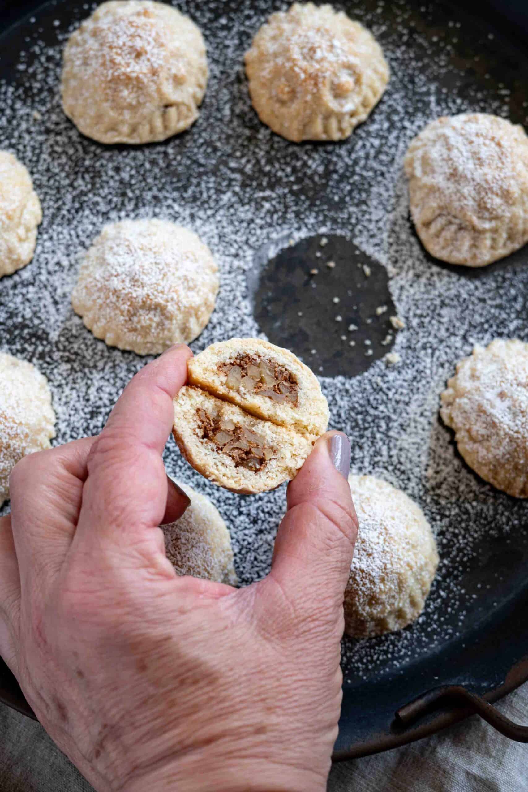 Holding a walnut-filled maamoul, split open down the middle.