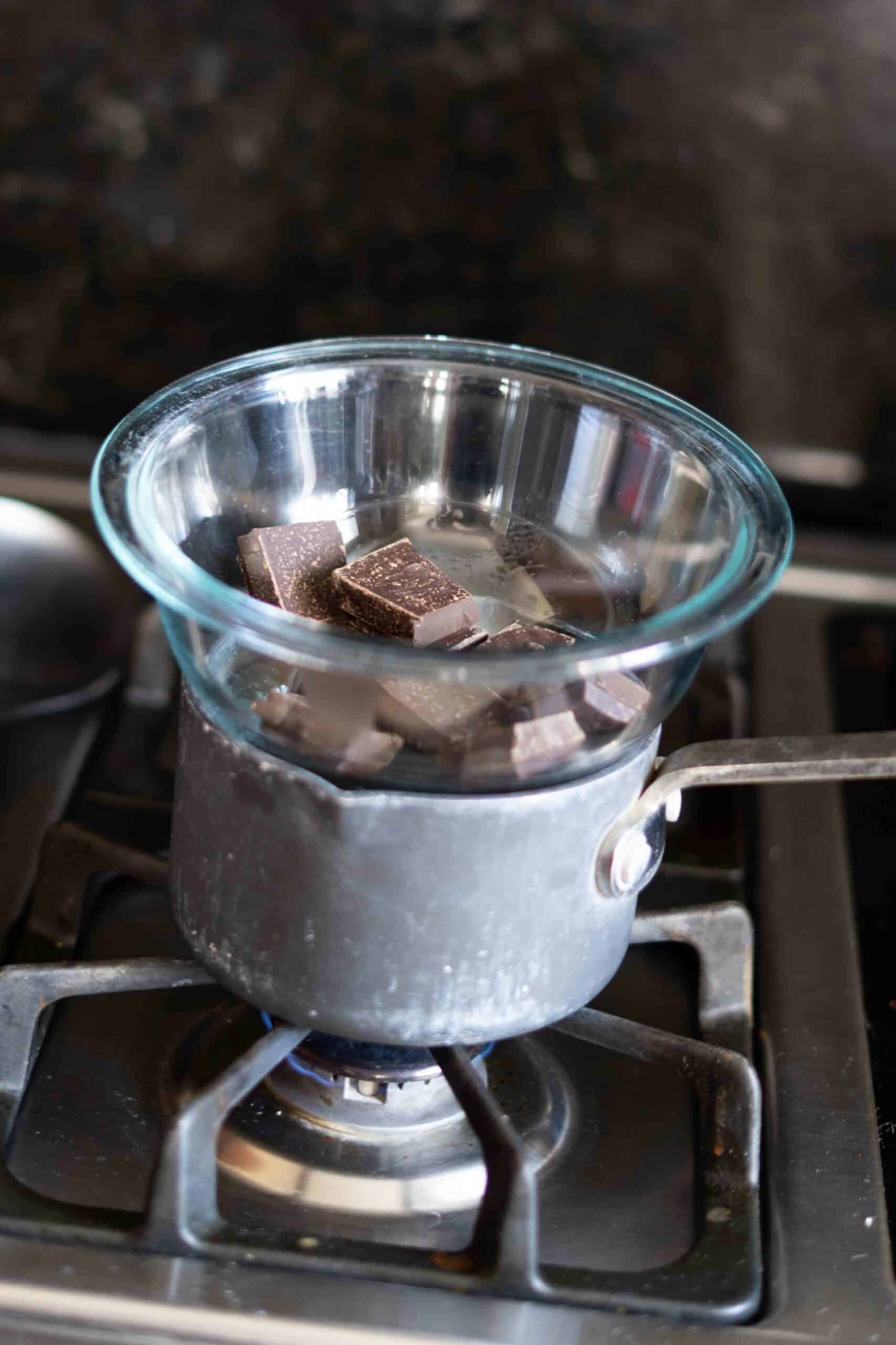 A bowl of chocolate bars sits over a small pot of boiling water on the stove to melt the chocolate.