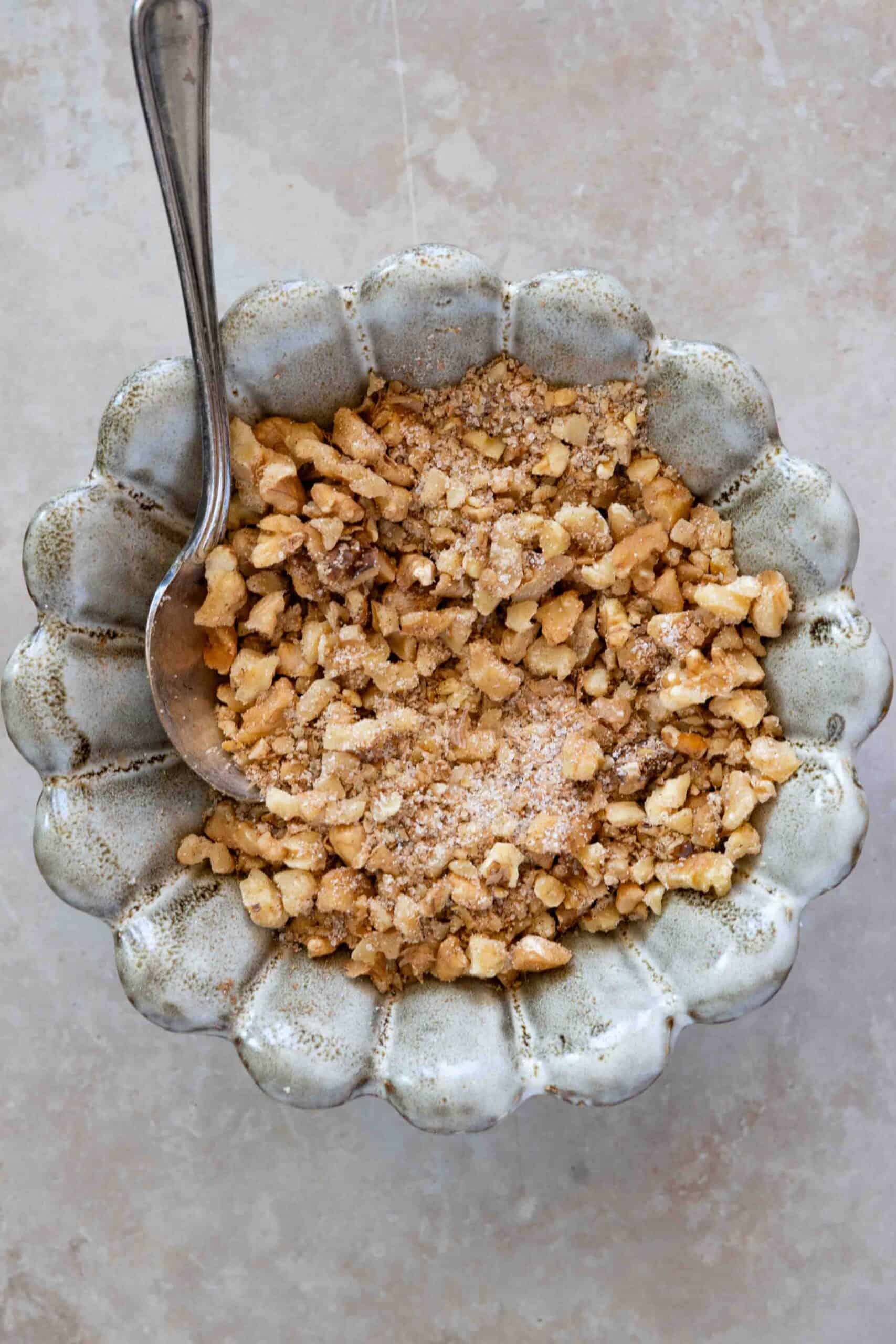 Walnut filling in a bowl, contains chopped walnuts, granulated sugar, cinnamon and nutmeg powder all mixed together.