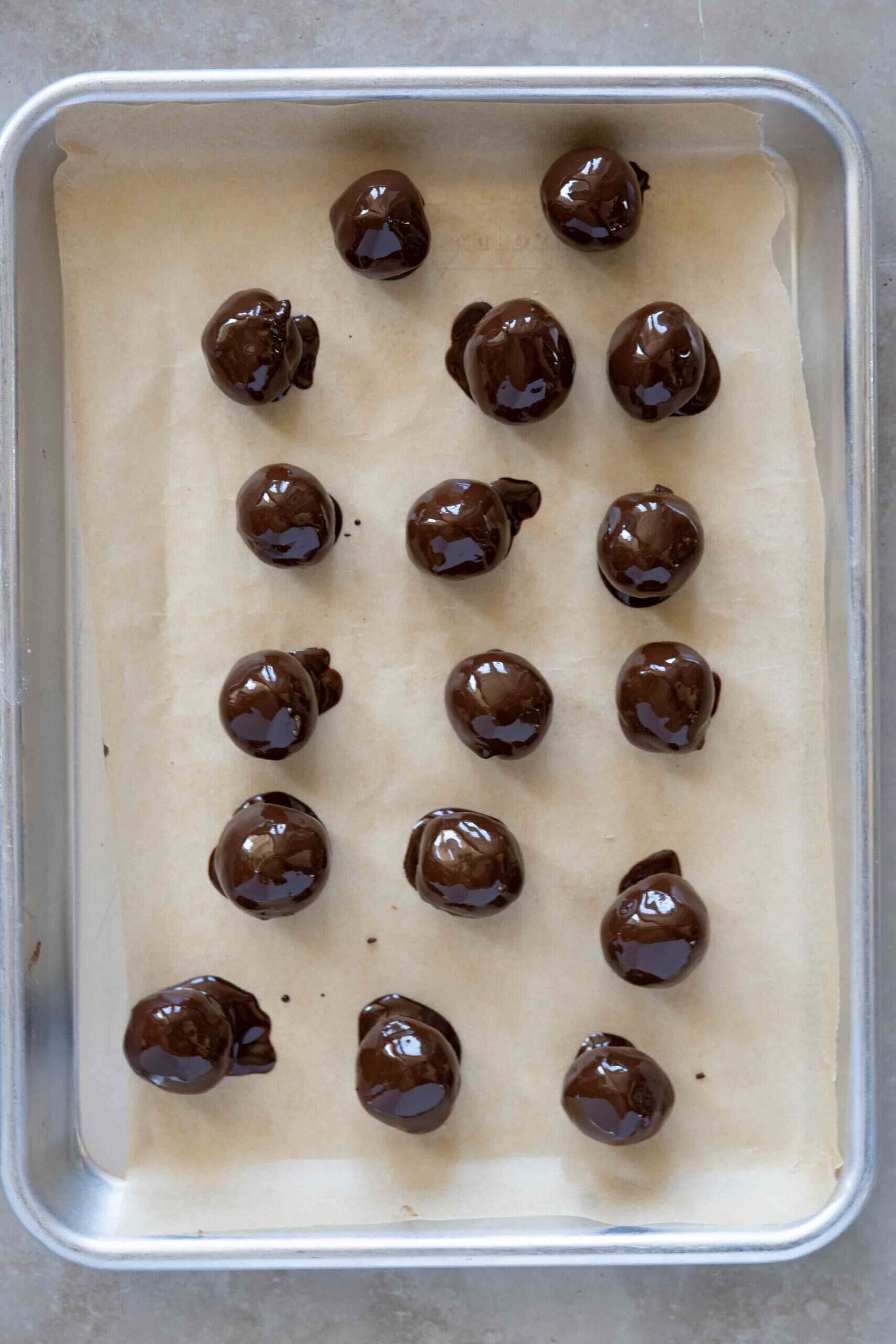 Tahini chocolate balls coated with melted chocolate, placed on a tray lined with parchment paper.
