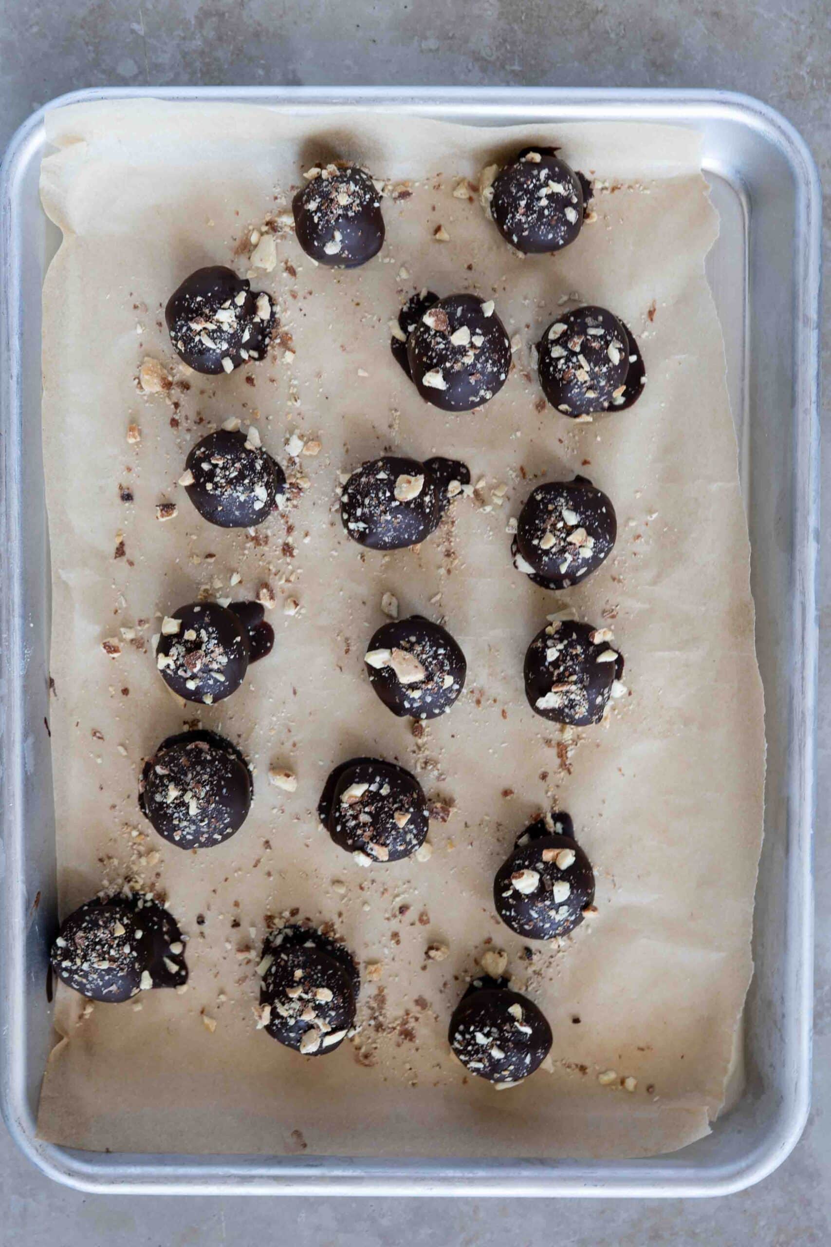 Tahini chocolate balls sprinkled with walnut placed on a tray lined with parchment paper.