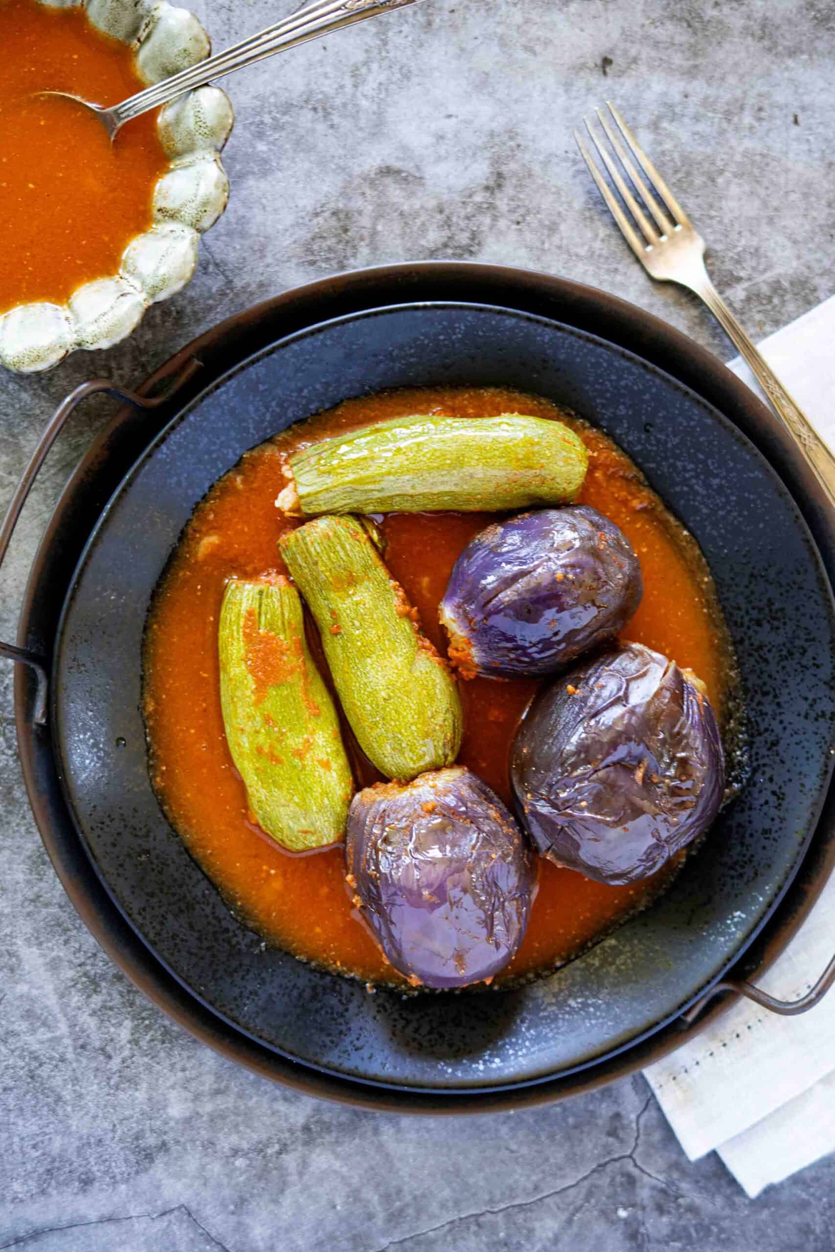 Stuffed eggplants and zucchini in tomato sauce, next to a bowl with tomato juice.
