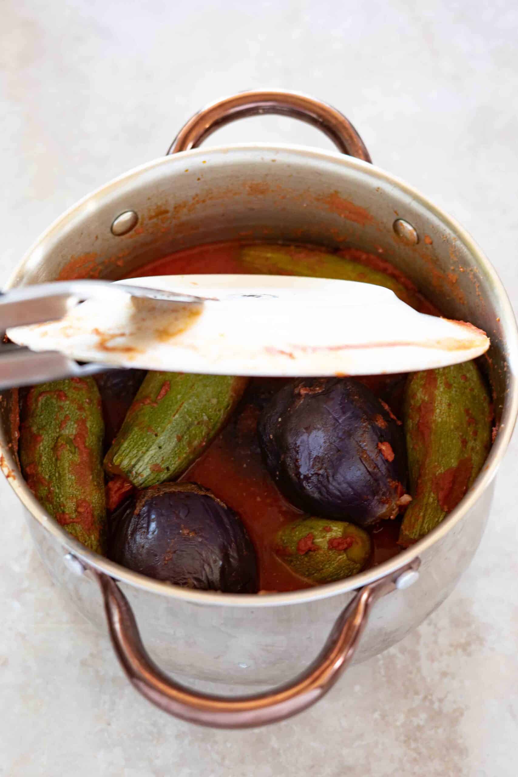 Using kitchen tongs, carefully removing the plate from over the stuffed eggplants and zucchini.