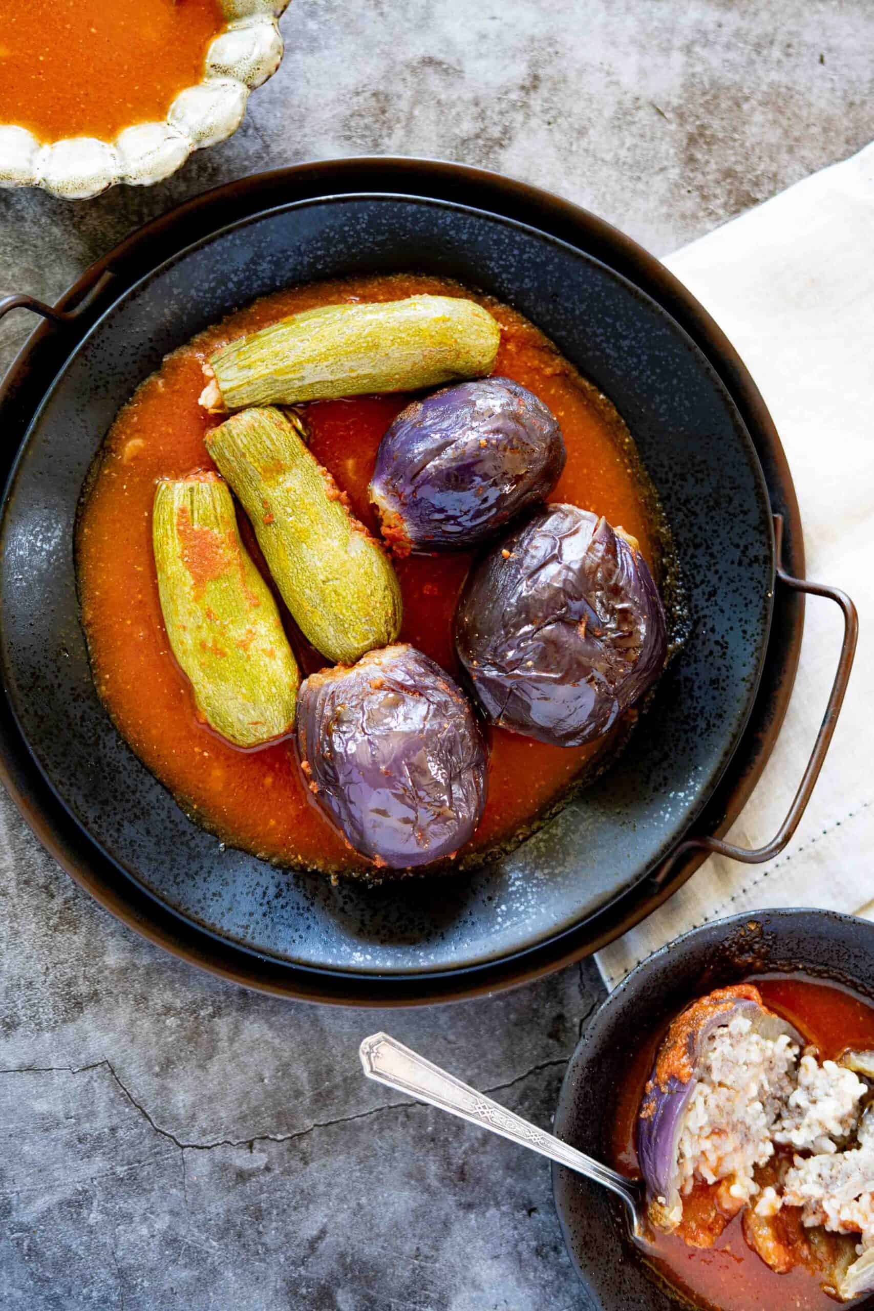 Stuffed eggplants and zucchini in tomato sauce, with one eggplant split open to reveal the filling.