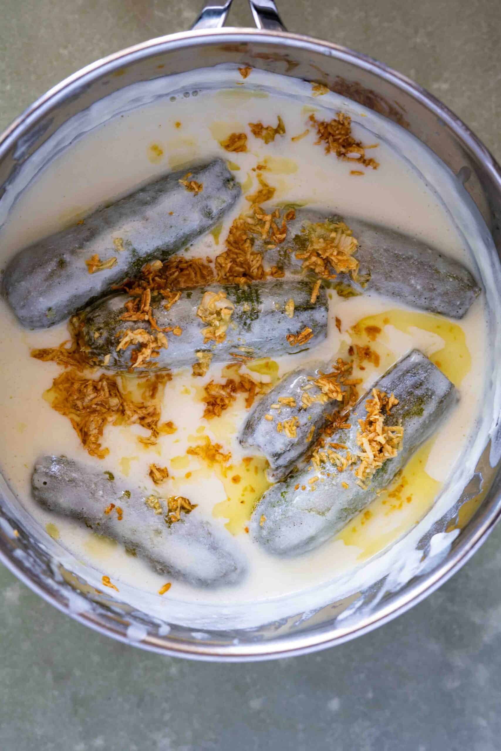 A close up photo for stuffed zucchini in a pot simmered in a creamy yogurt sauce and topped with caramelized garlic.