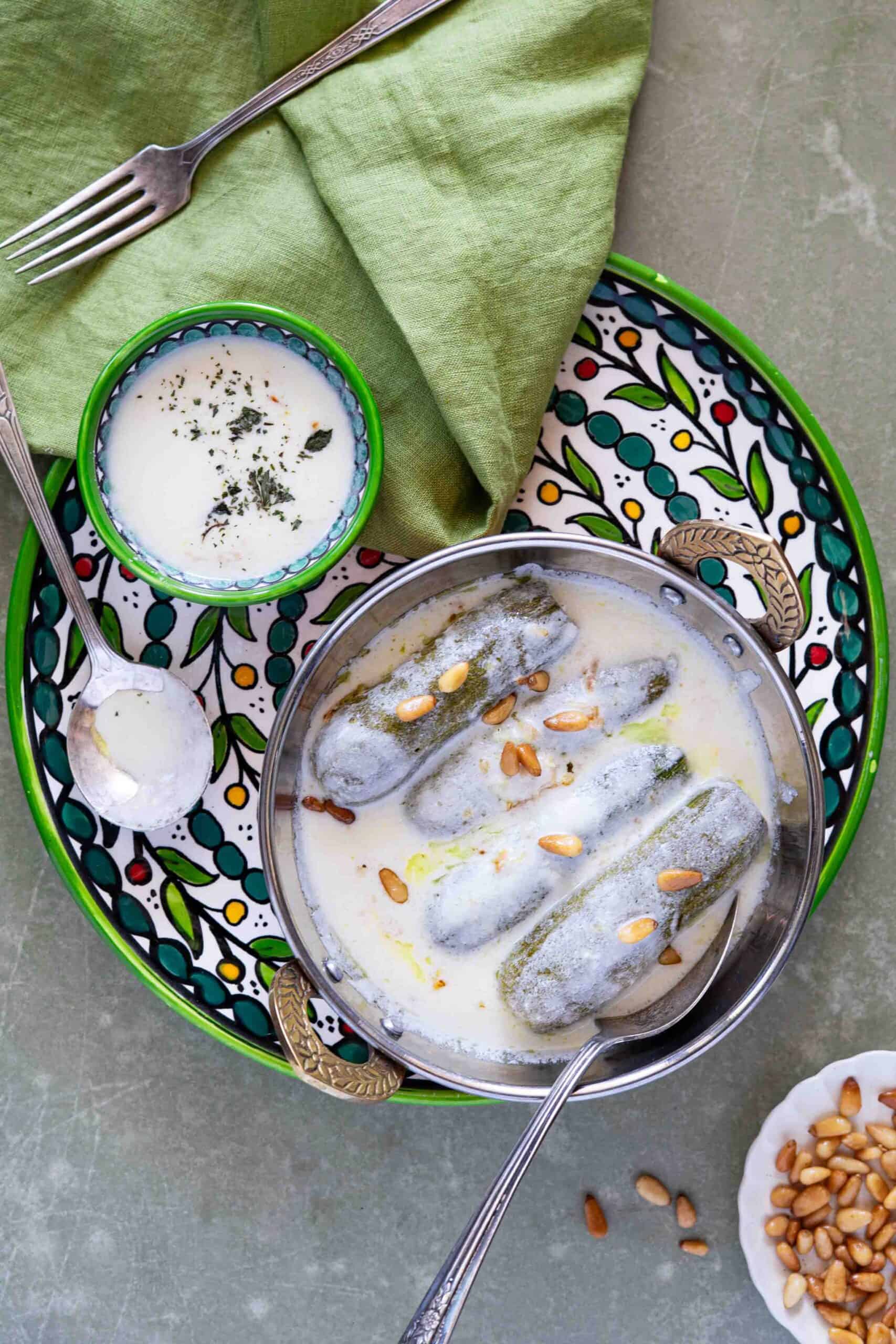 Kousa Bil Laban served on a plate, topped with toasted pine nuts and accompanied by a small bowl of creamy yogurt sauce.