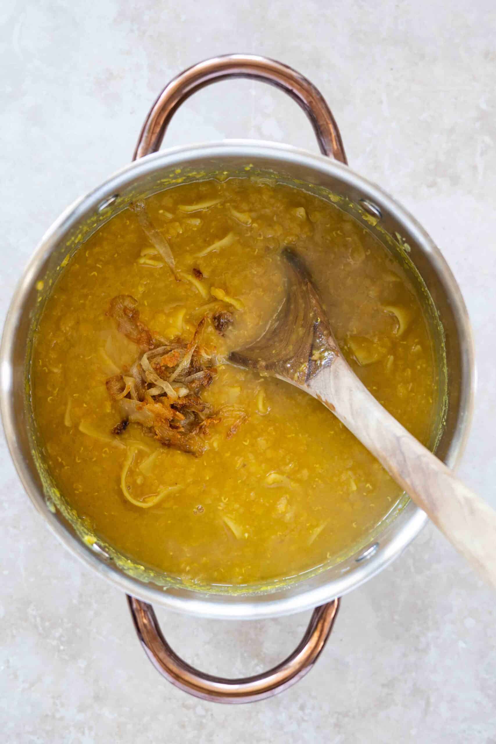 Adding a portion of caramelized onions to the simmering lentils and past in a pot