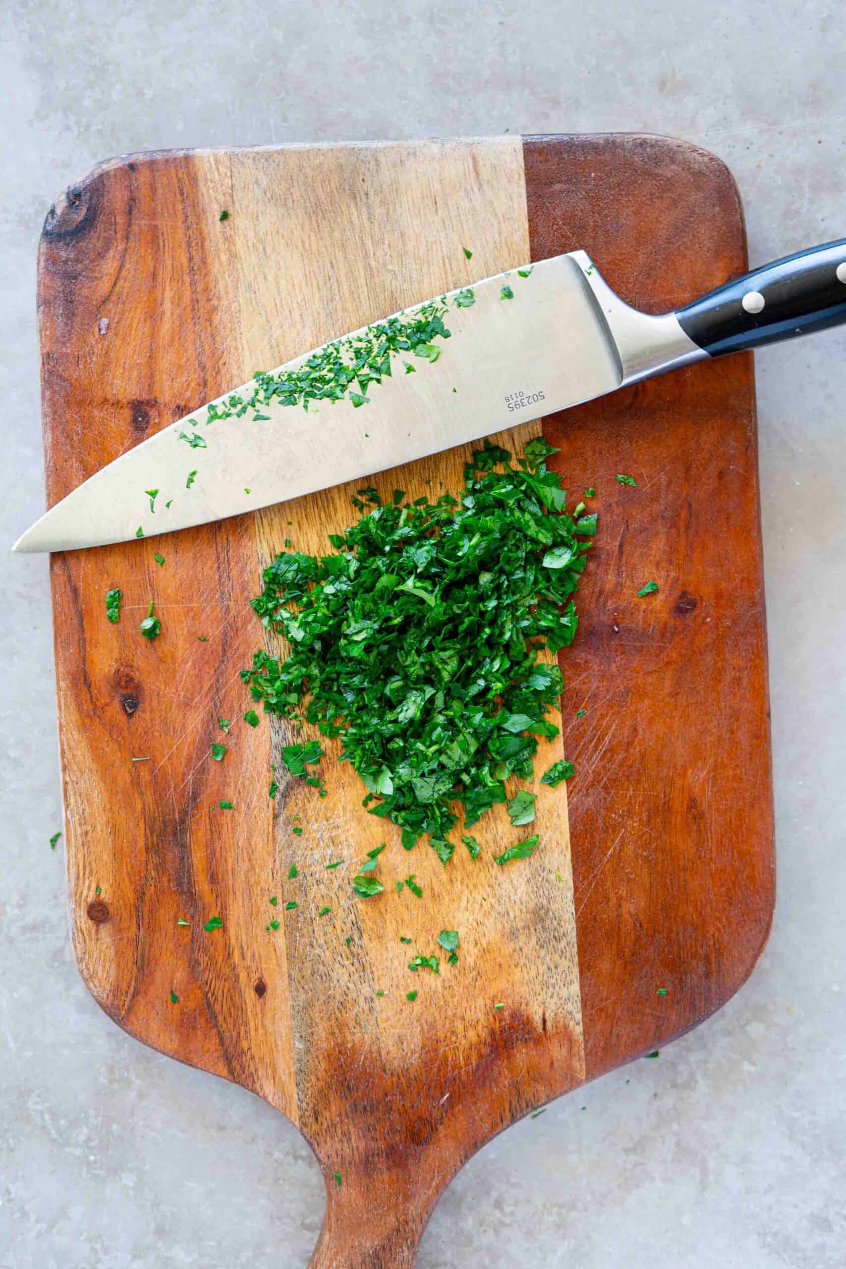 Fresh parsley finely chopped on a wooden cutting board with a sharp knife.