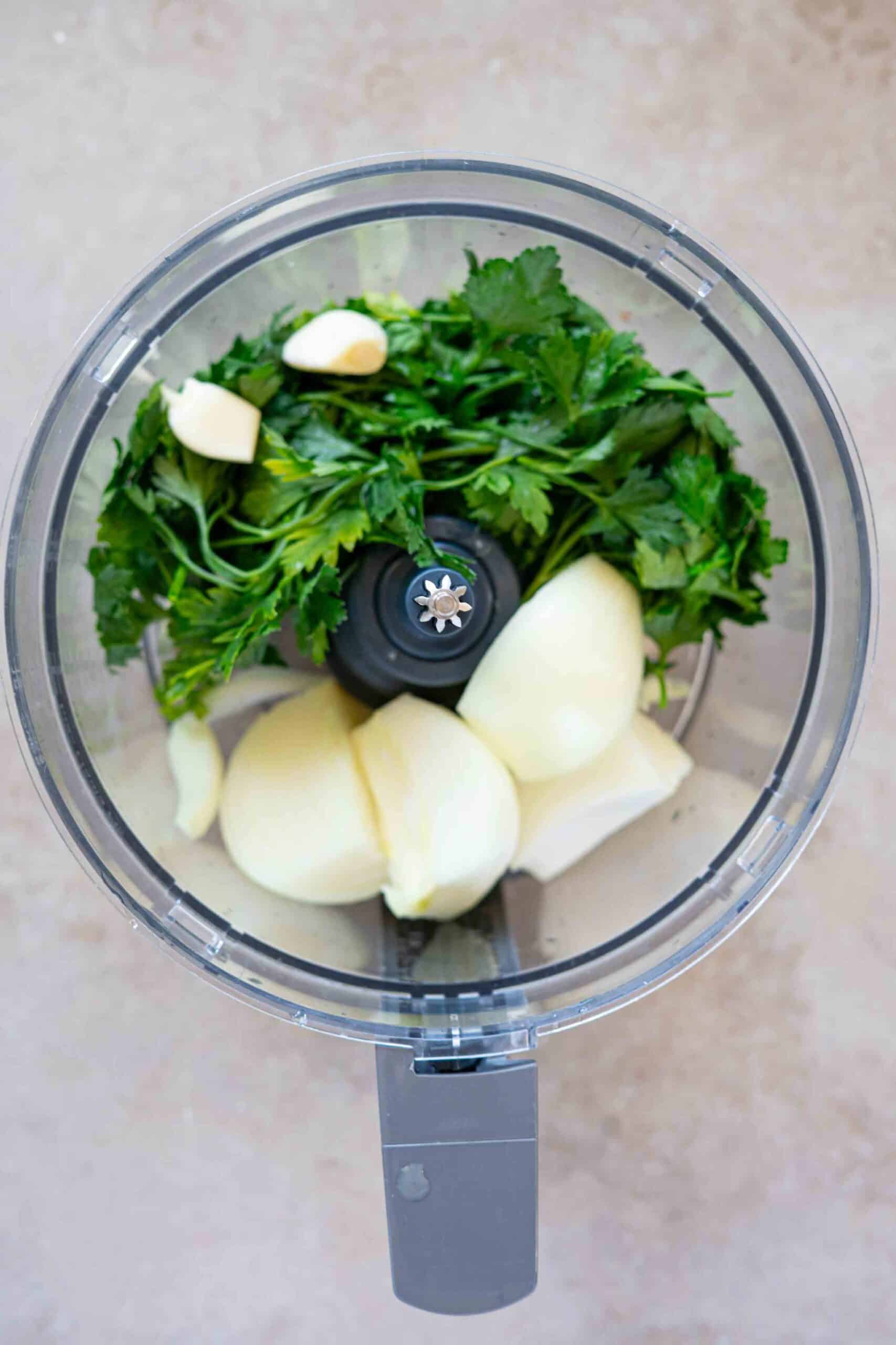 Peeled onions, garlic cloves and parsley leaves in a food processor.