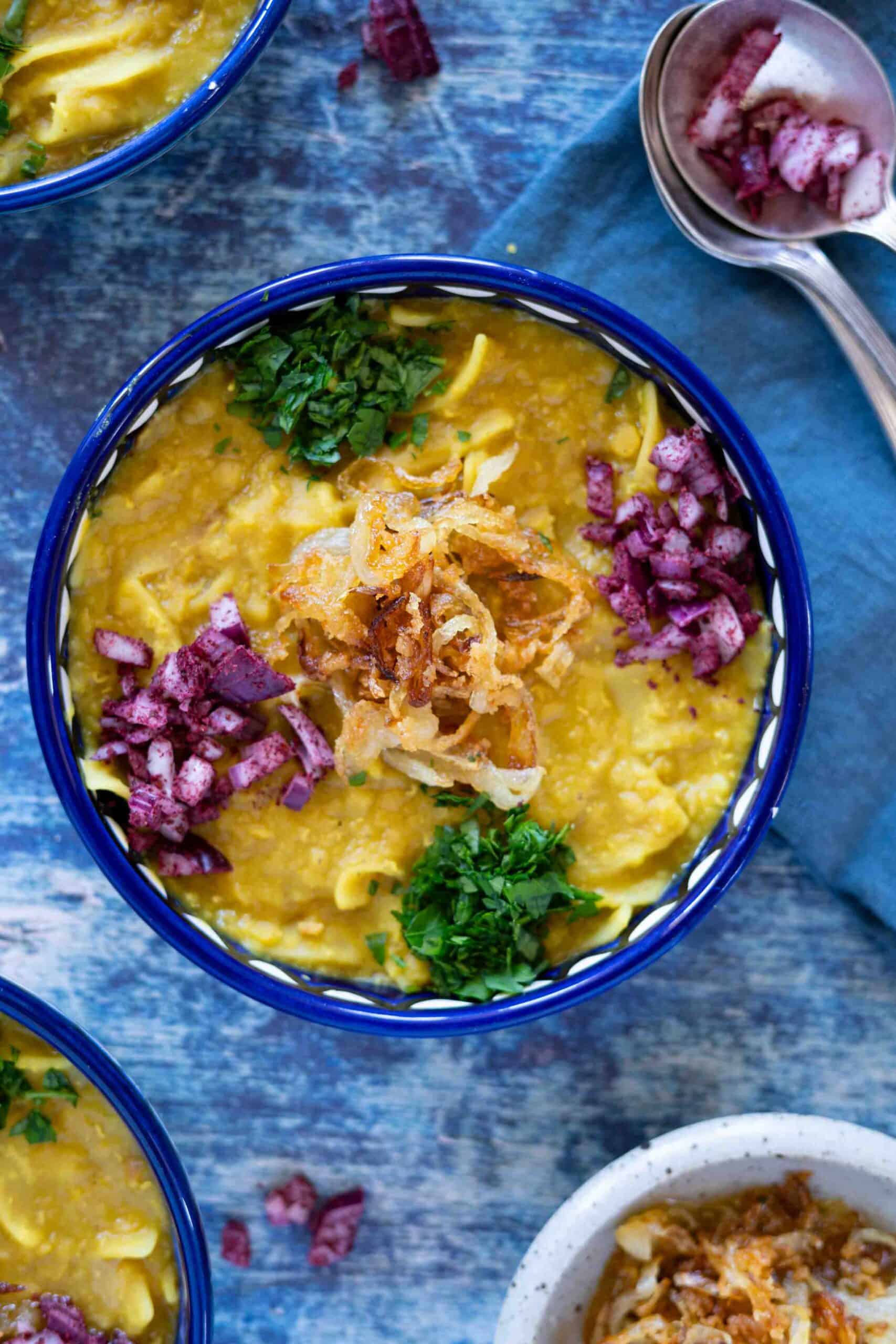 A plate of Palestinian red lentils with pasta (rishtayeh) garnished with caramelized onions, fresh parsley, diced red onions mixed with sumac.