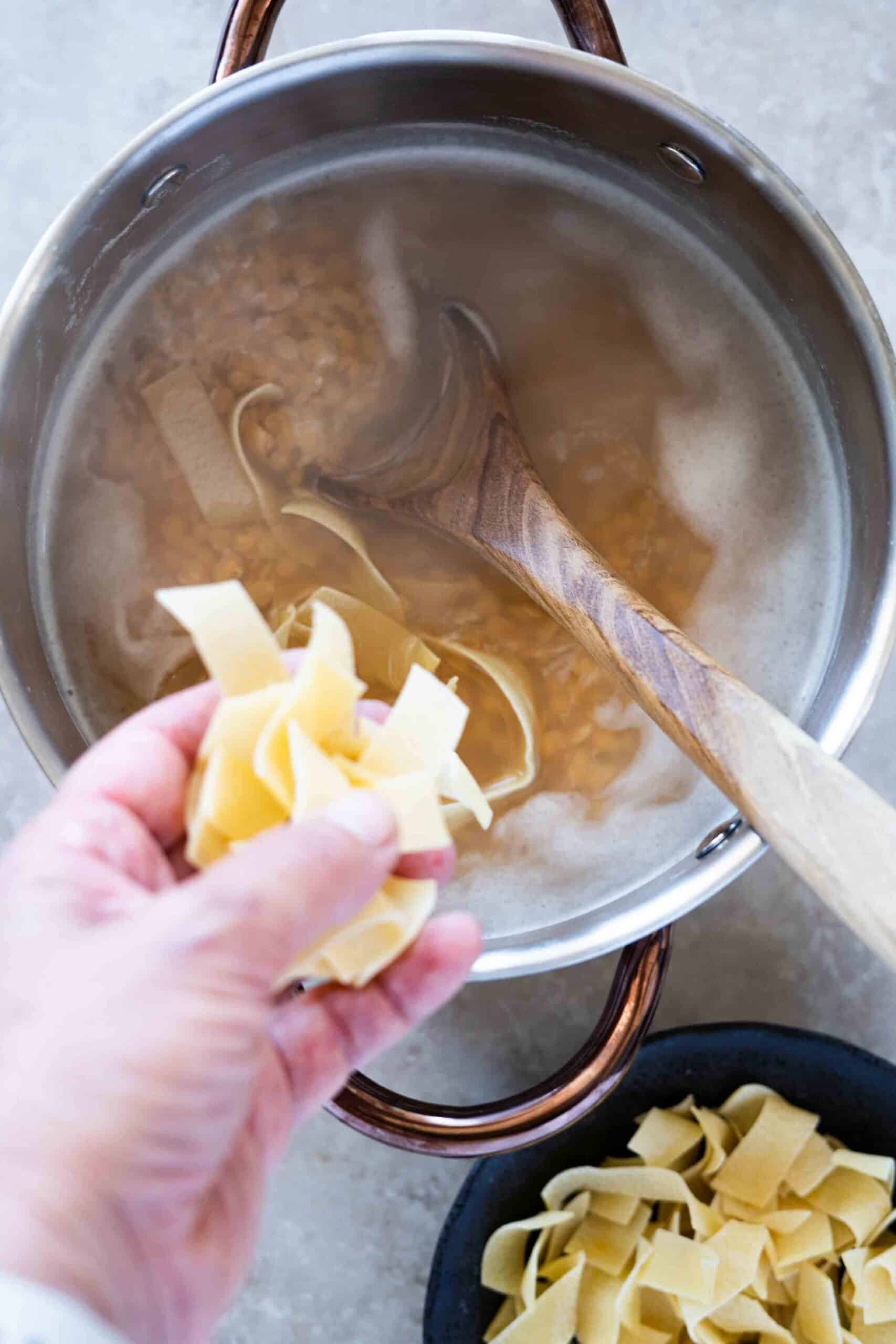 Adding pasta to a pot of simmering red lentils.